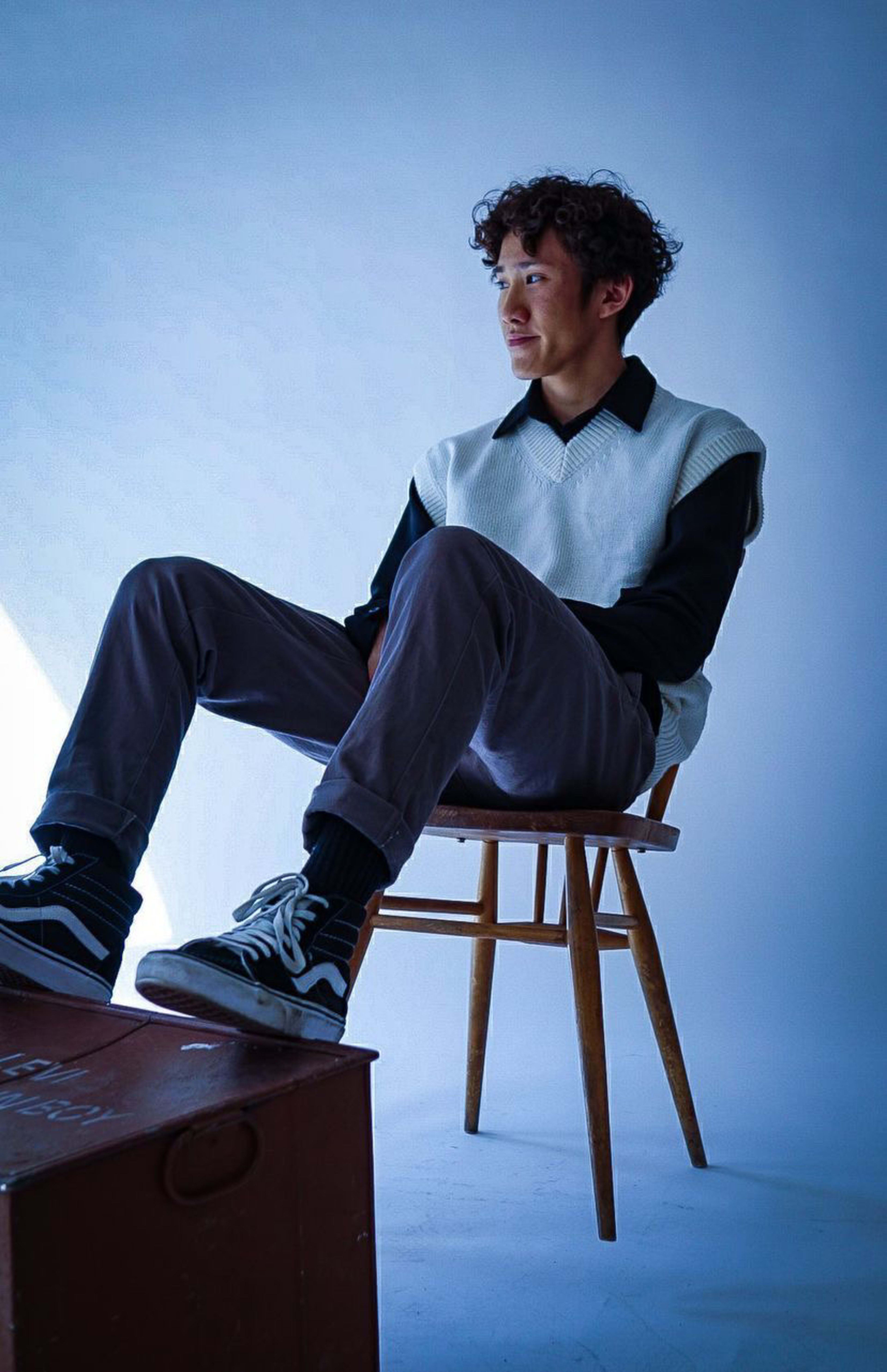 A man in blue sitting in a chair with his feet on a black suitcase during a photo shoot.