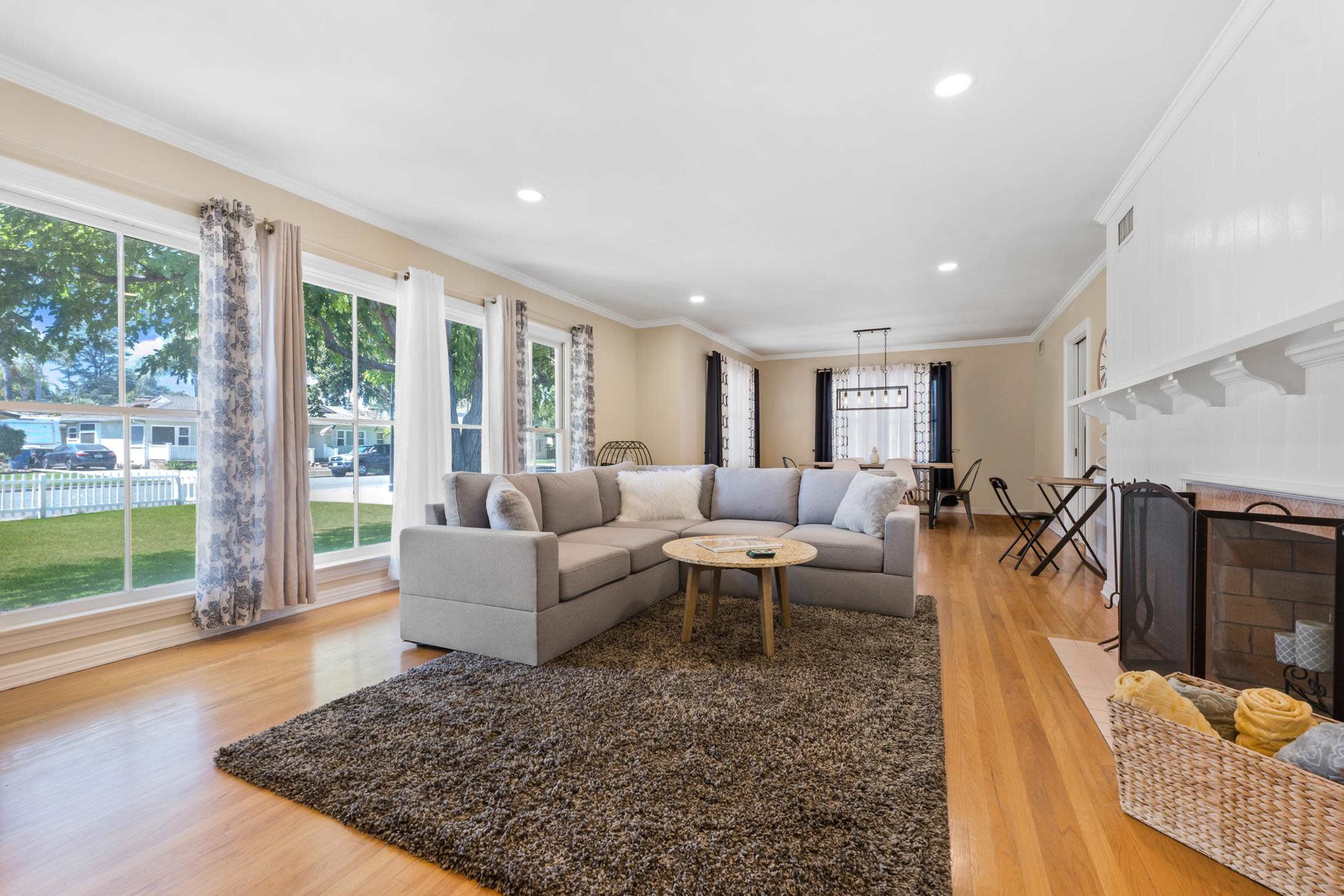A spacious living room features a large sectional sofa, a round table, and large windows that let in ample natural light.