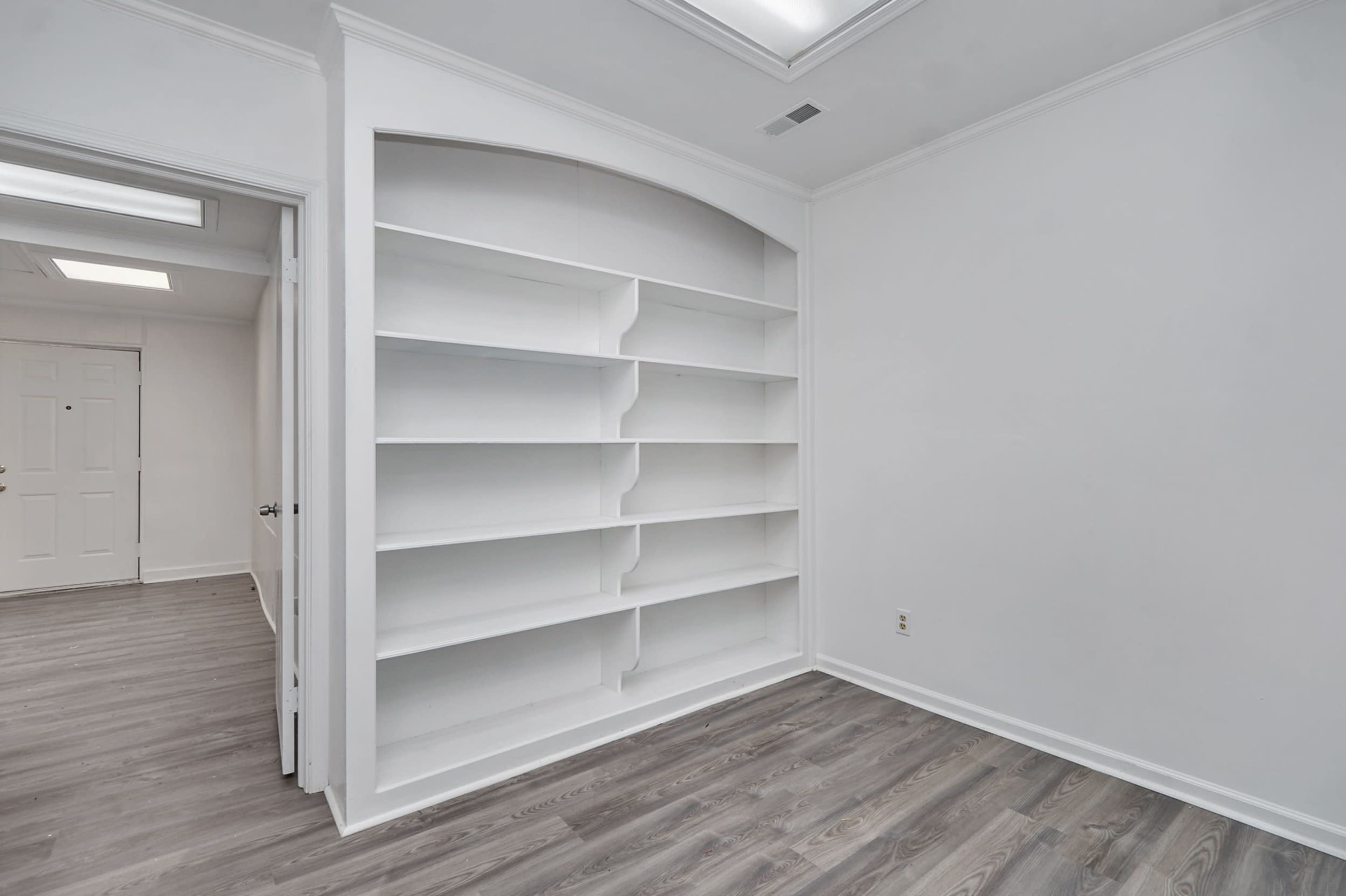 A room with a large white built-in shelving unit against one wall and a door leading to another room.