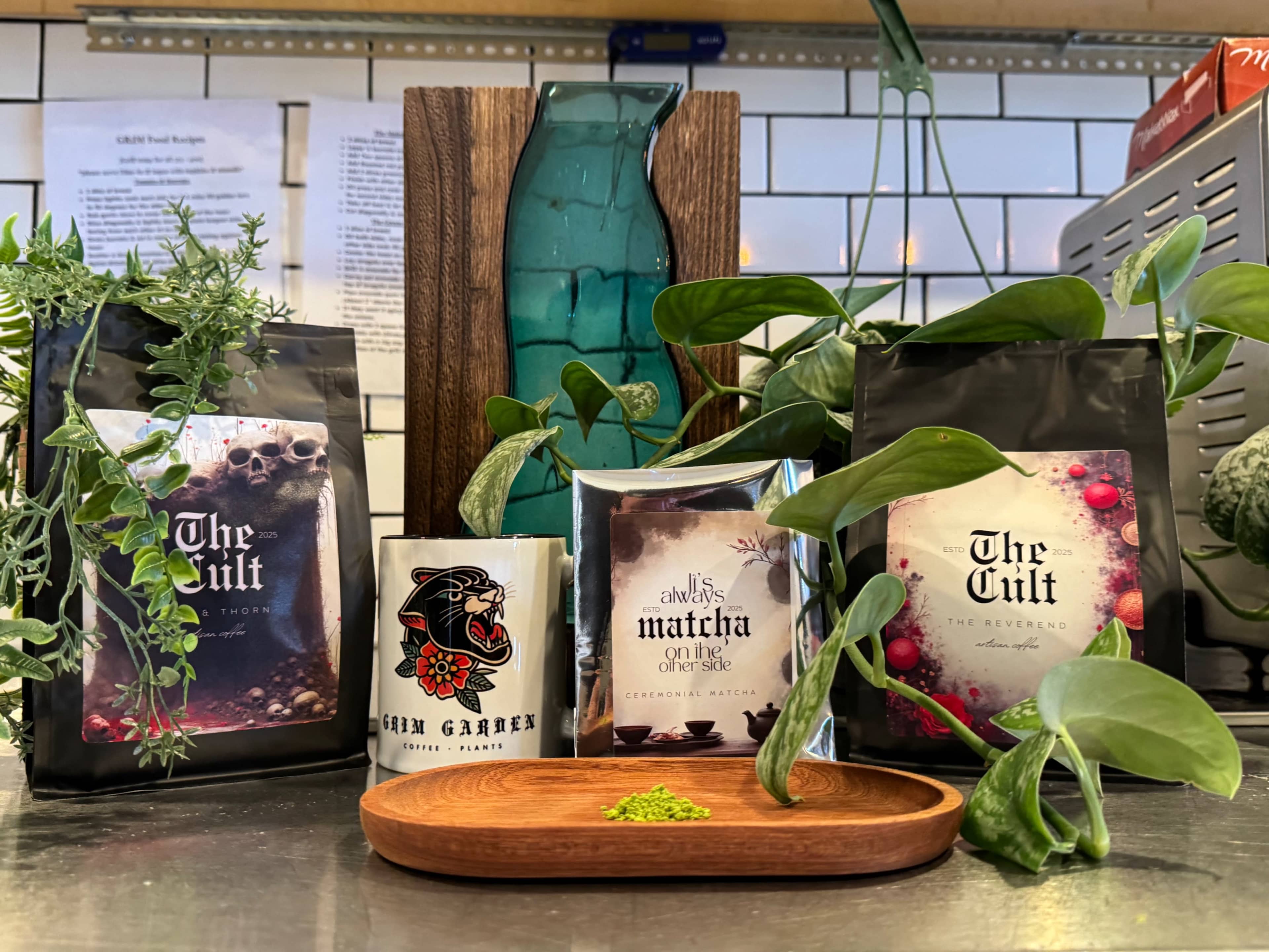 The image displays several bags of tea and matcha products arranged on a counter alongside a wooden dish and decorative plants.