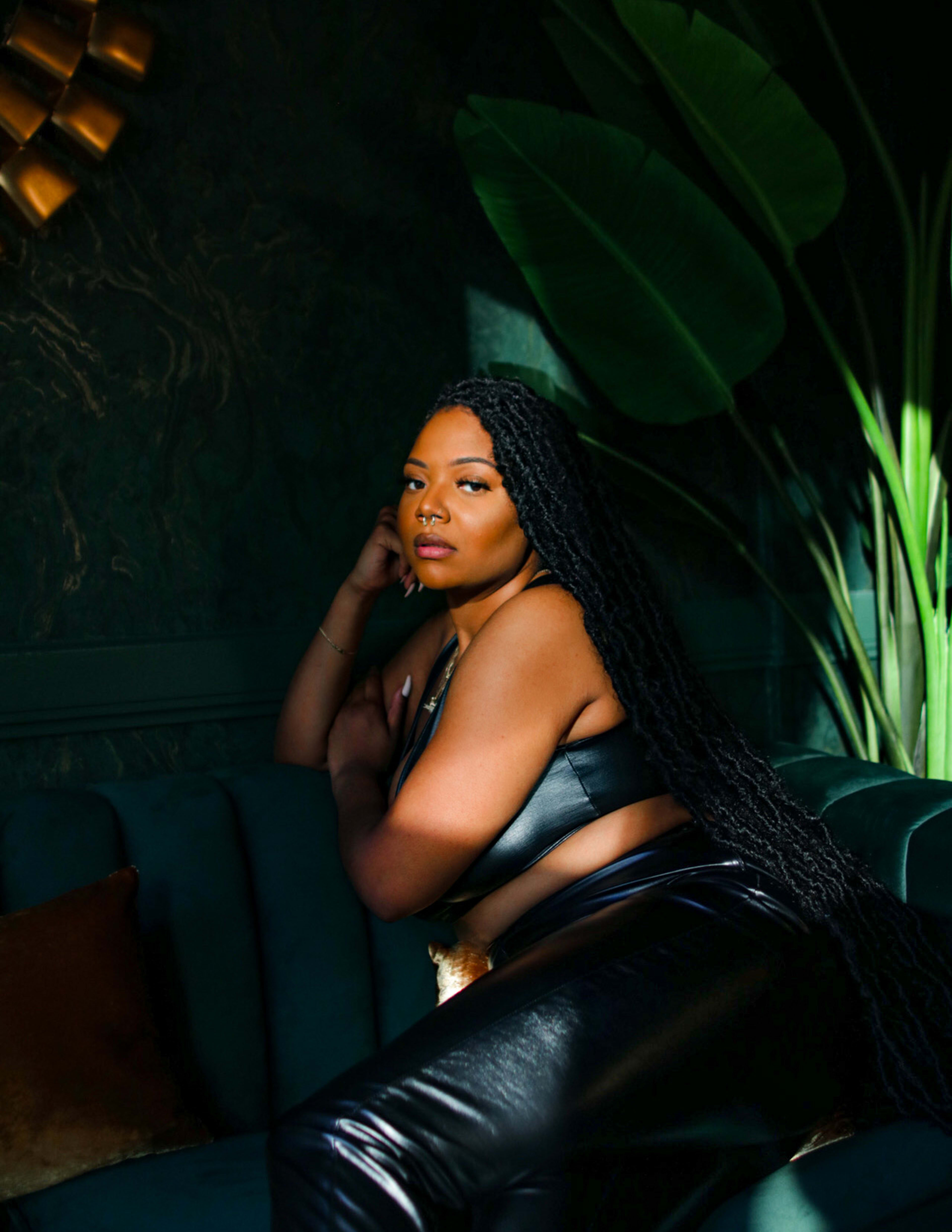 A woman posing for a photo shoot on top of a couch surrounded by green plants.