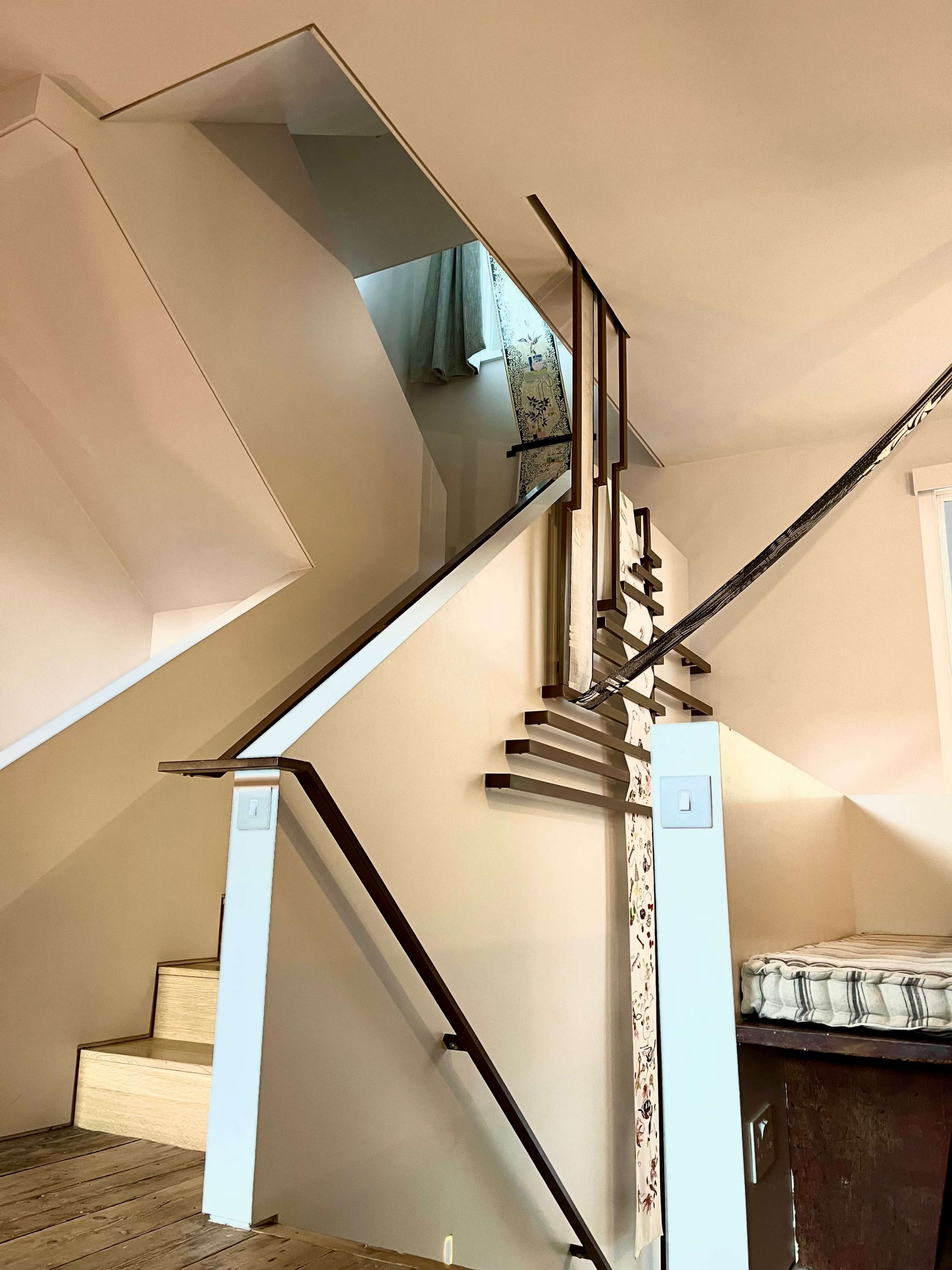 A staircase with an angular design leads to an upper level, featuring wooden steps and metal railings, illuminated by natural light.