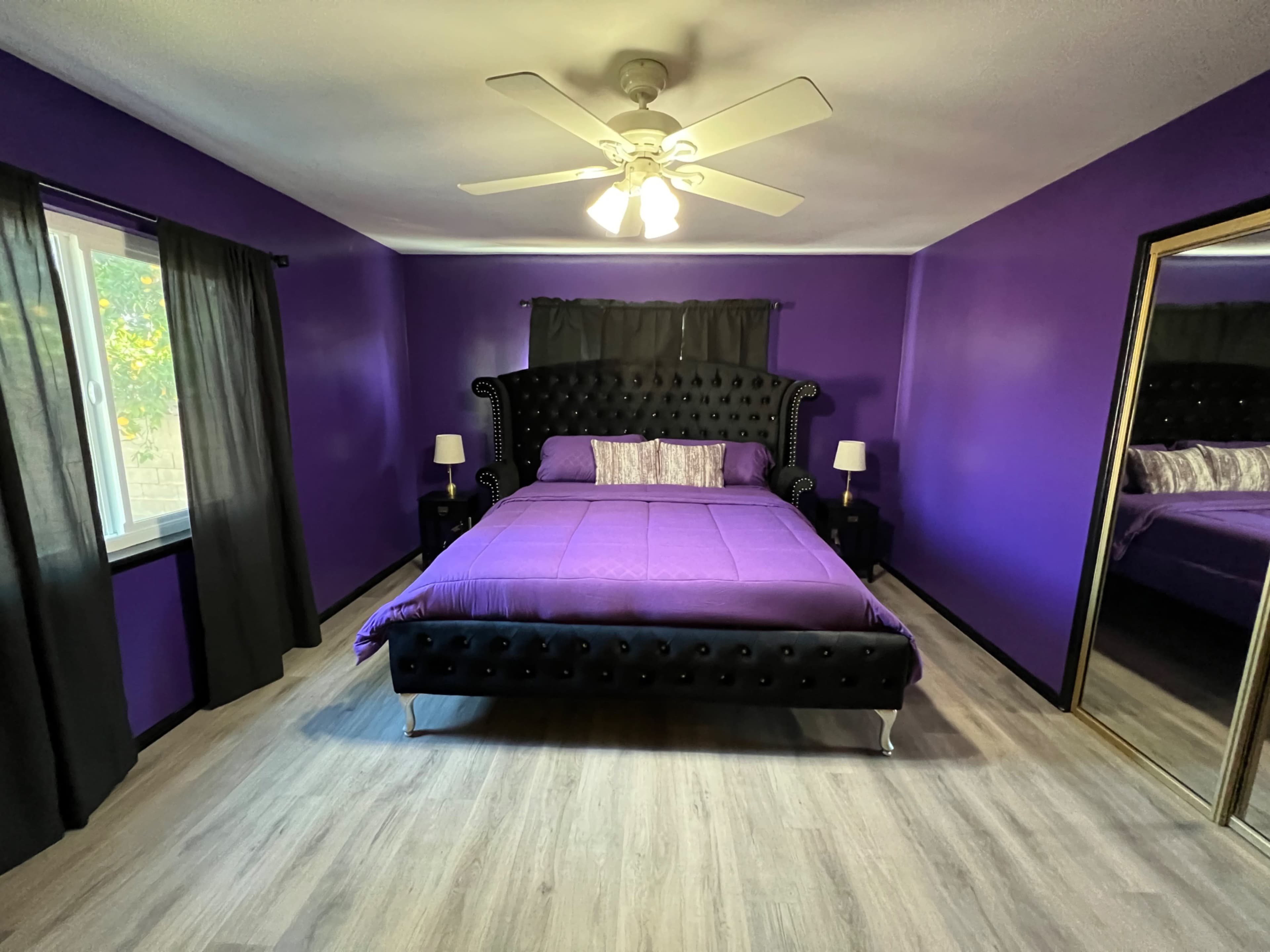 A bedroom with purple walls, a black tufted bed, and two bedside lamps beside the bed.