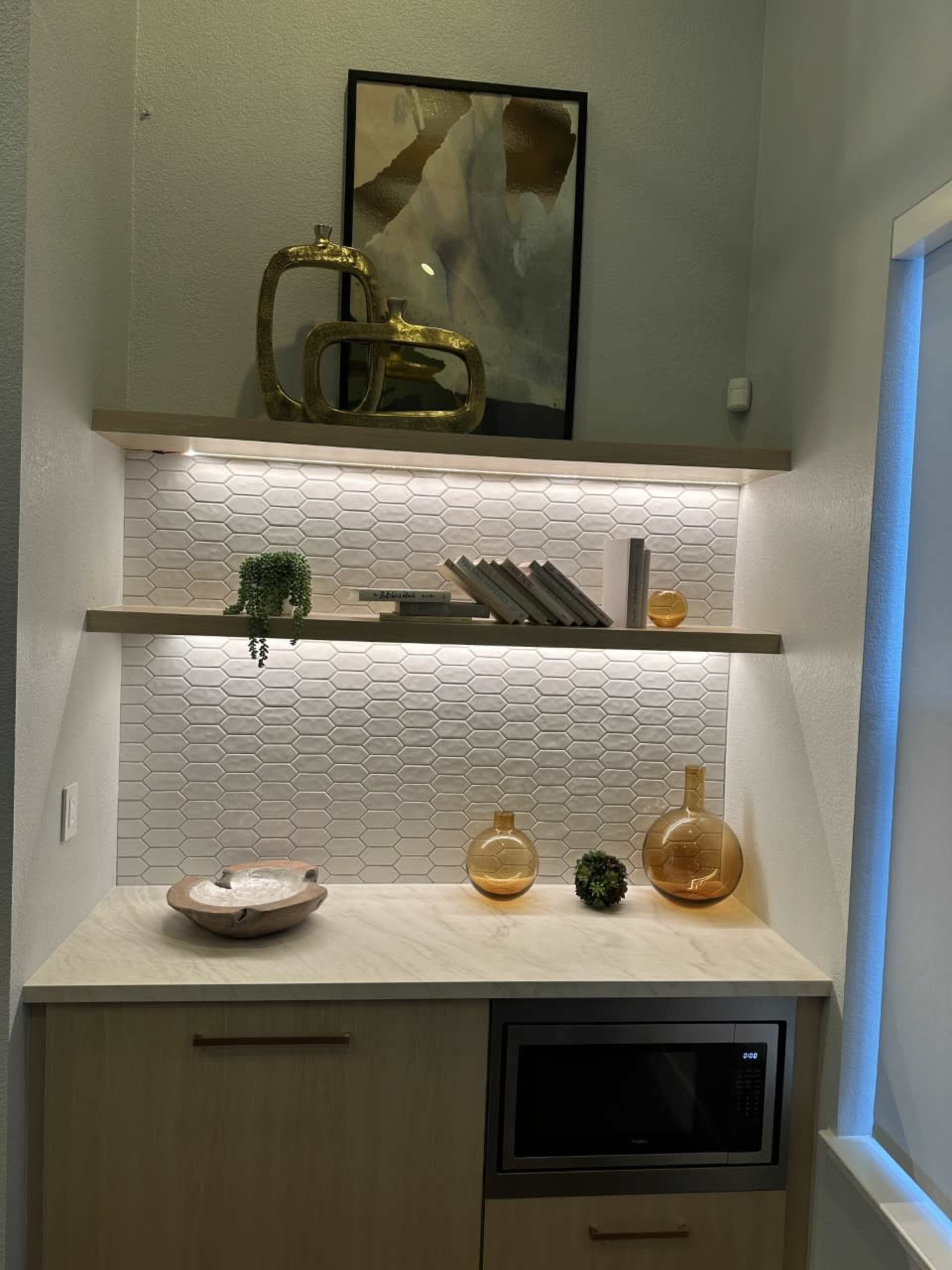 A minimalist shelving unit with decorative items, a small microwave, and a marble countertop in a well-lit space.