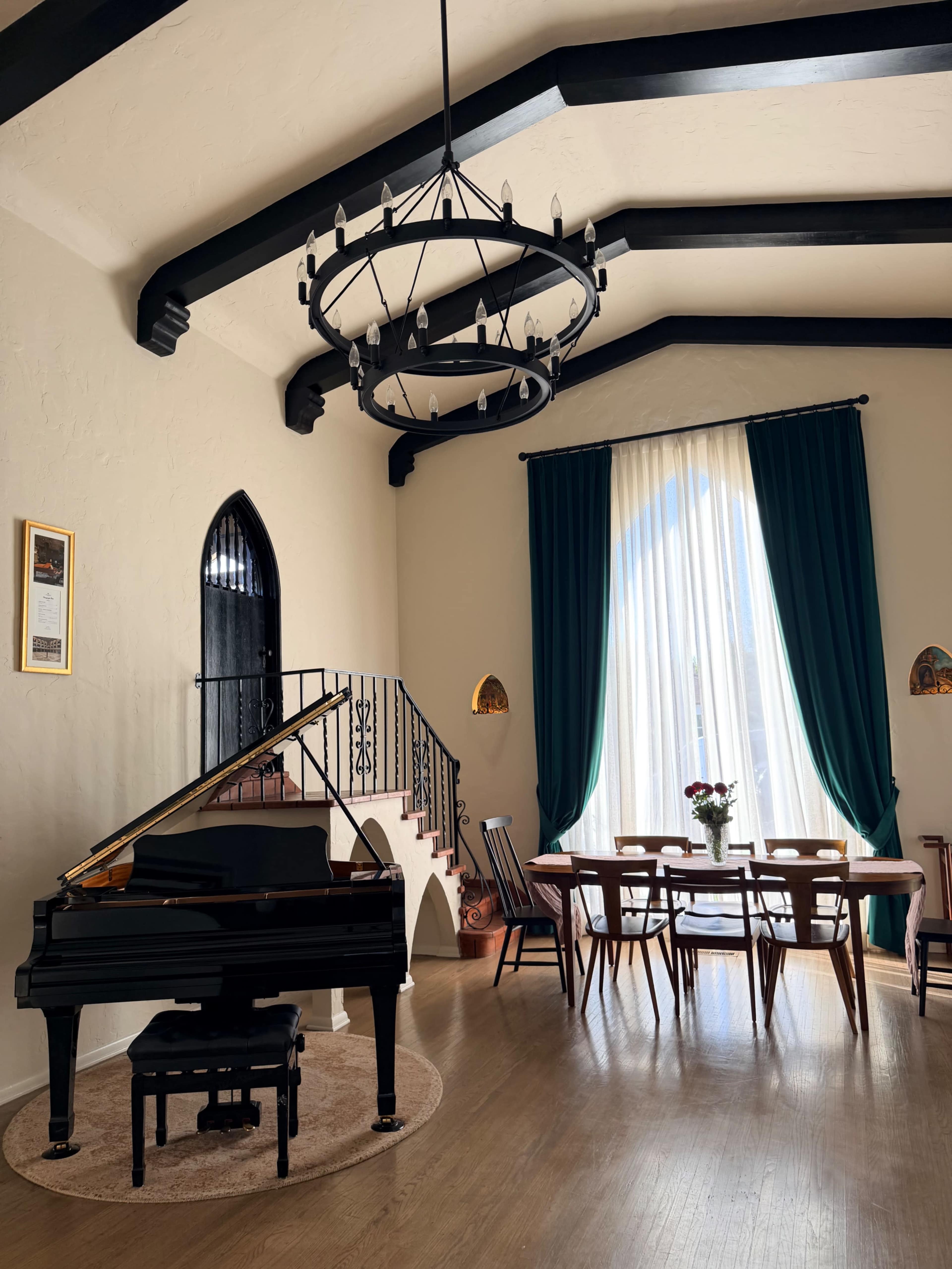 The image shows a spacious room featuring a grand piano, a dining table with chairs, and large windows adorned with floor-length curtains.
