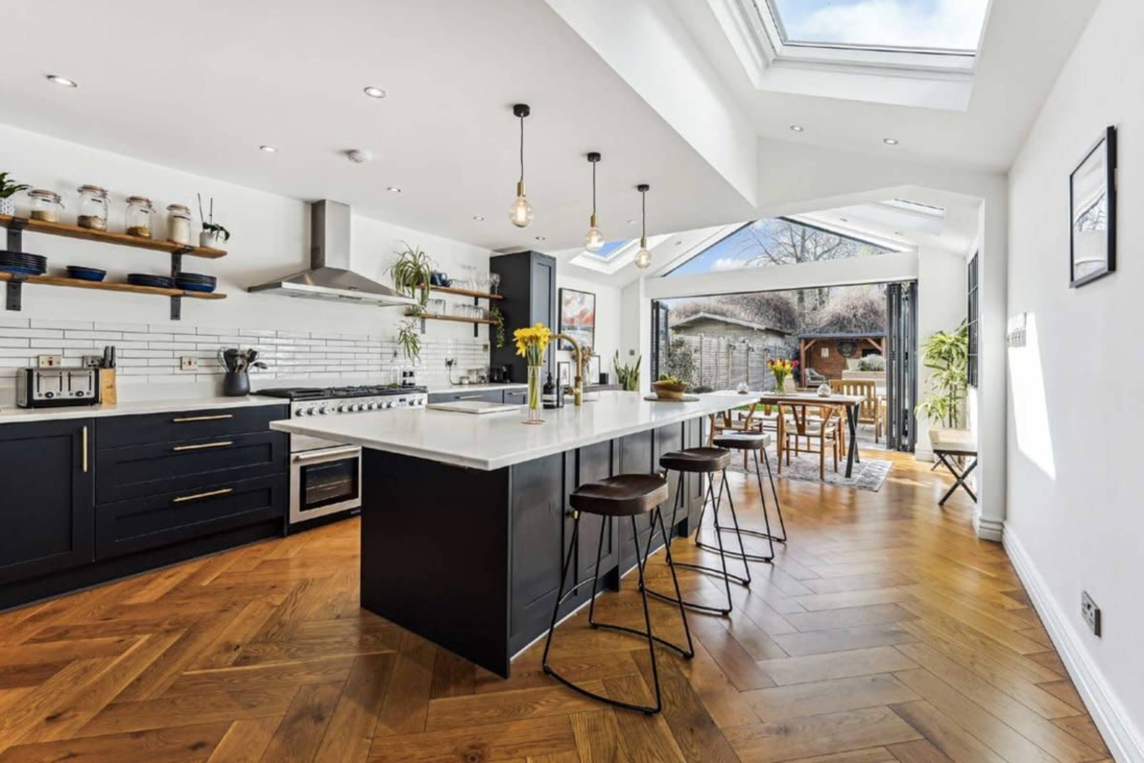 The modern kitchen features an island with bar stools, a stainless steel range, and large windows that provide natural light.