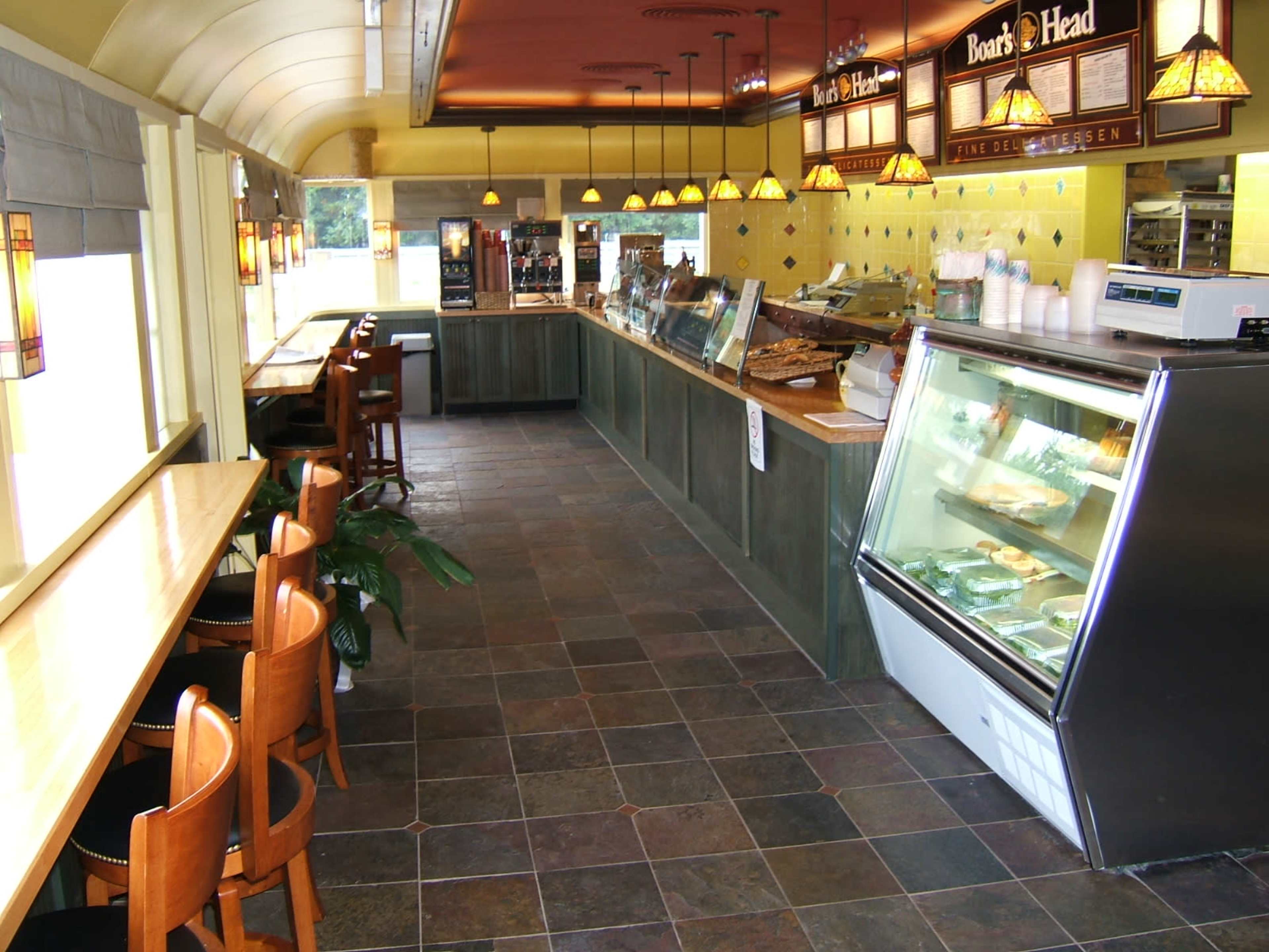 A deli interior with a long countertop, a refrigerated display case, and seating along one side.