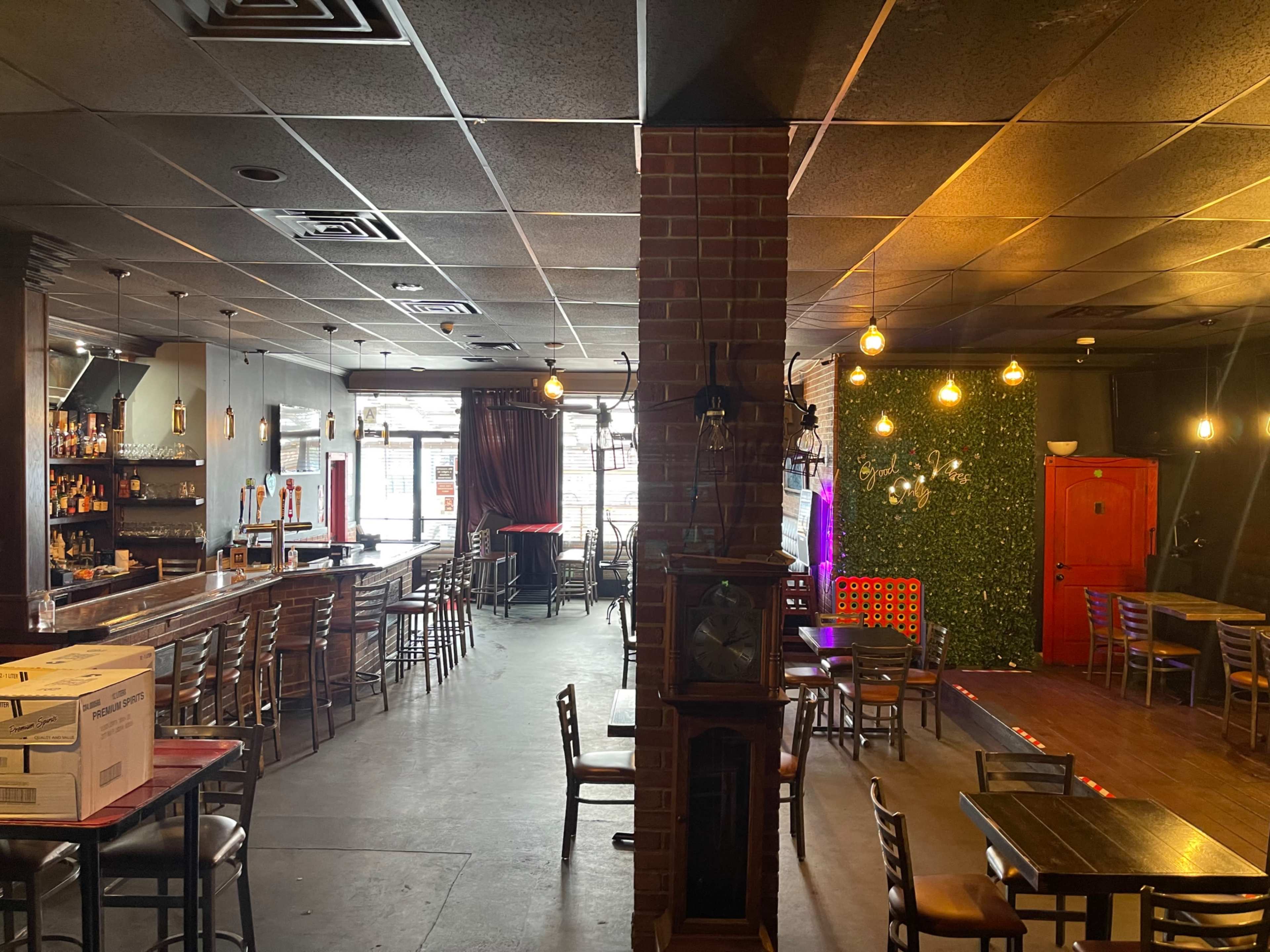 The image shows a bar area with seating, a dark wood bar counter on one side, and a lounge area with ambient lighting and a green wall on the other.