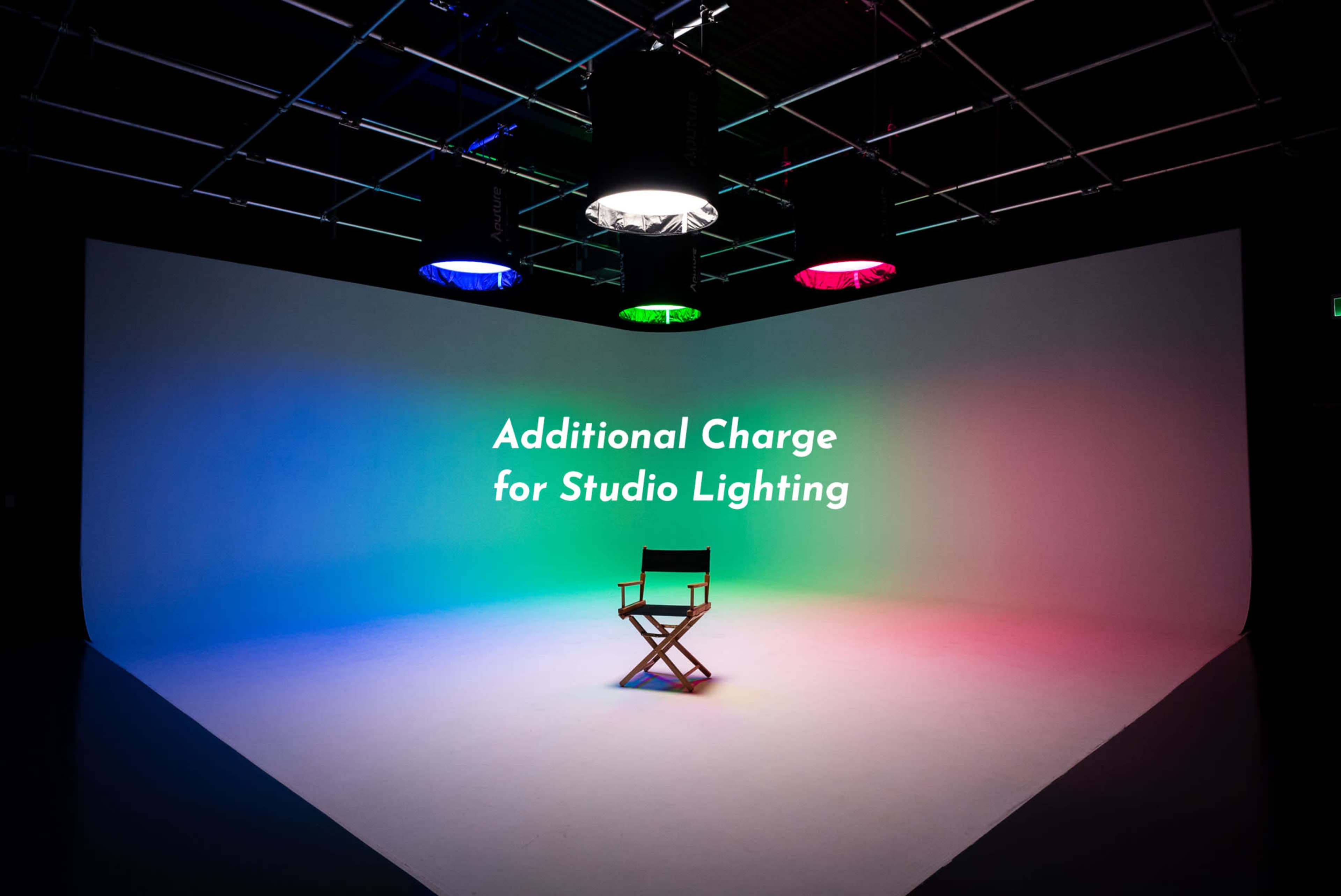 A director's chair sits in a brightly lit studio with colored lights and the words "Additional Charge for Studio Lighting" displayed on the wall.