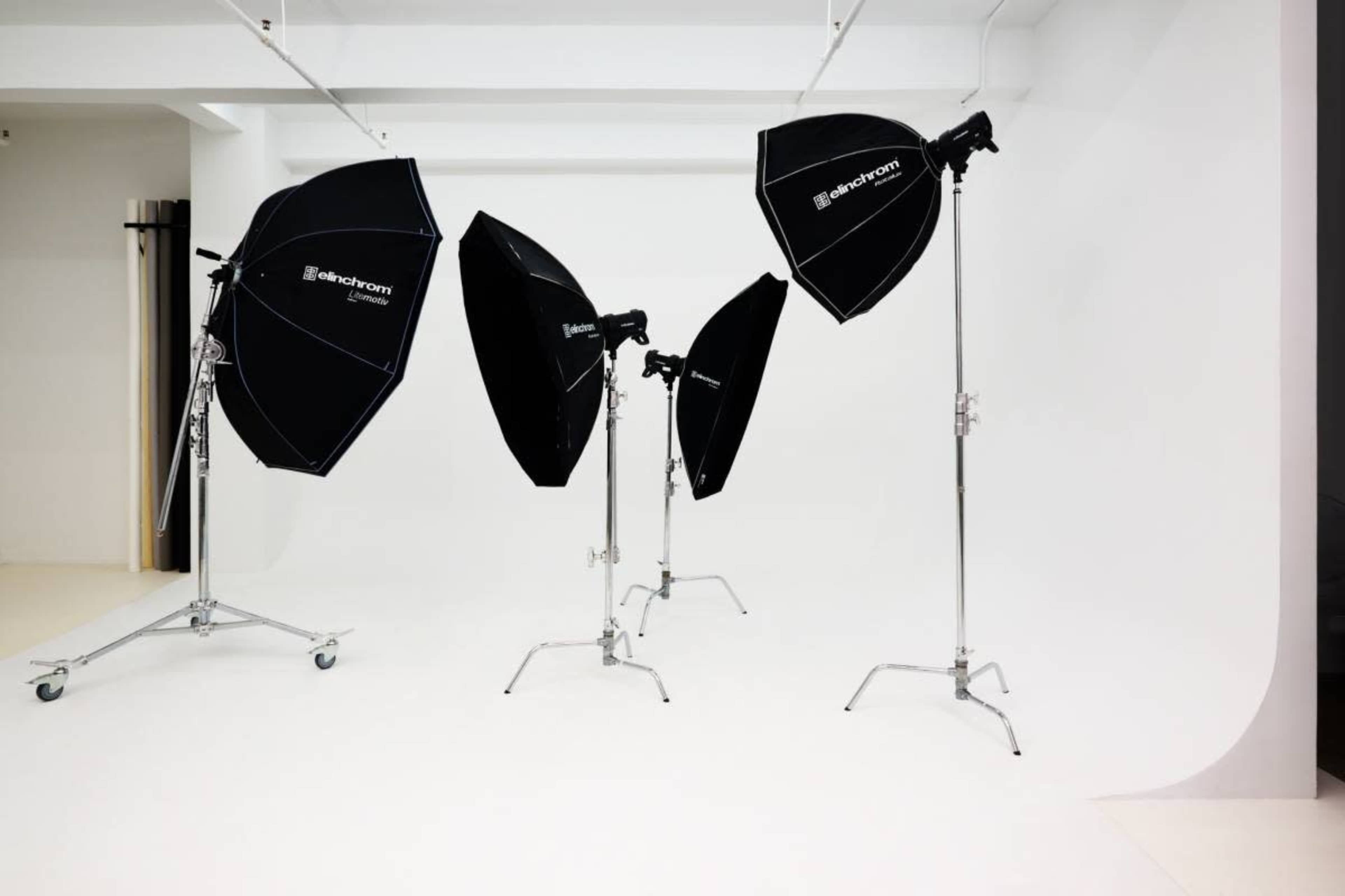 The image shows a photography studio featuring four black softbox lights on metal stands placed on a white background.