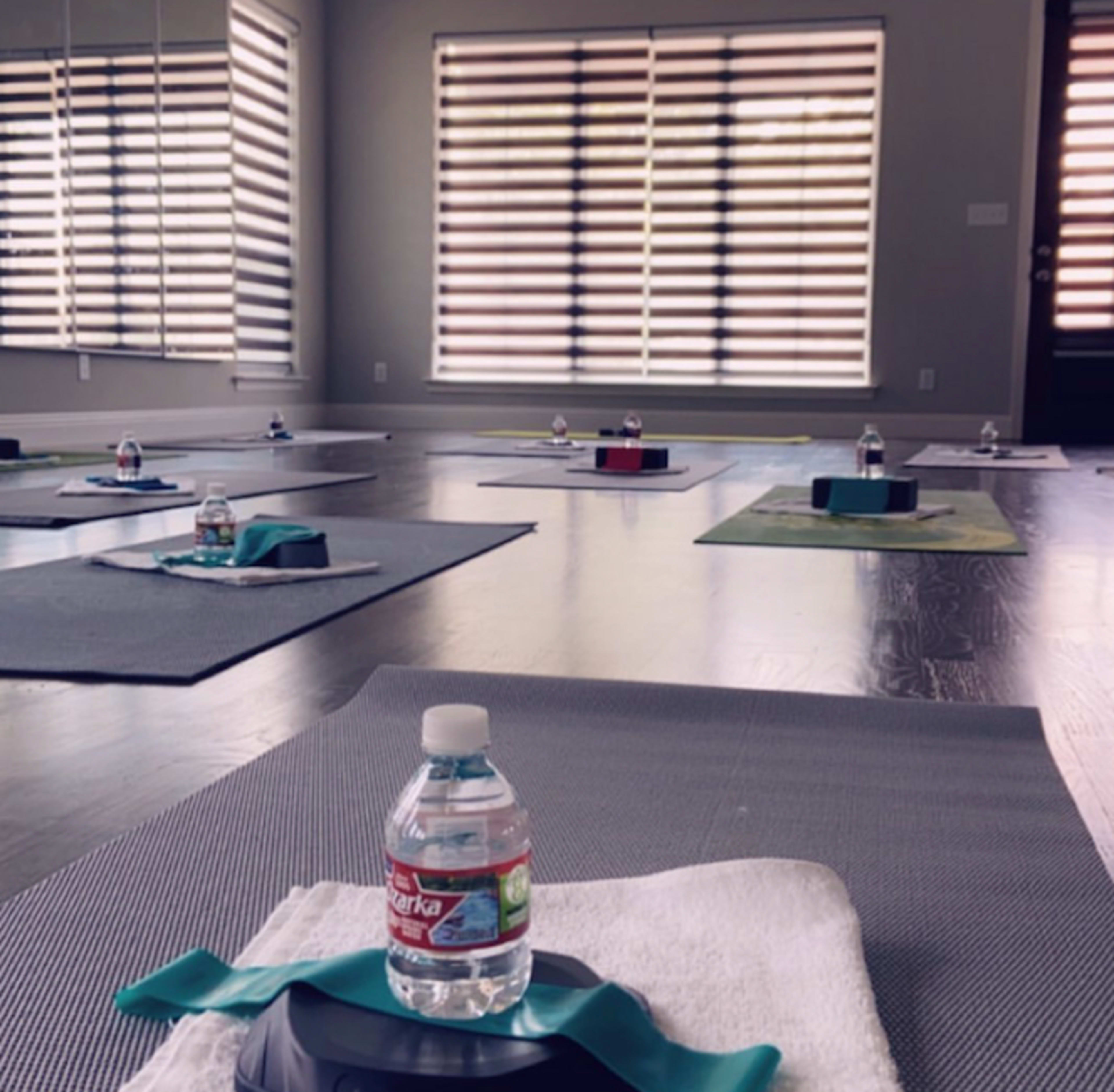 A spacious yoga studio features exercise mats arranged in a grid, each topped with a water bottle and a towel.
