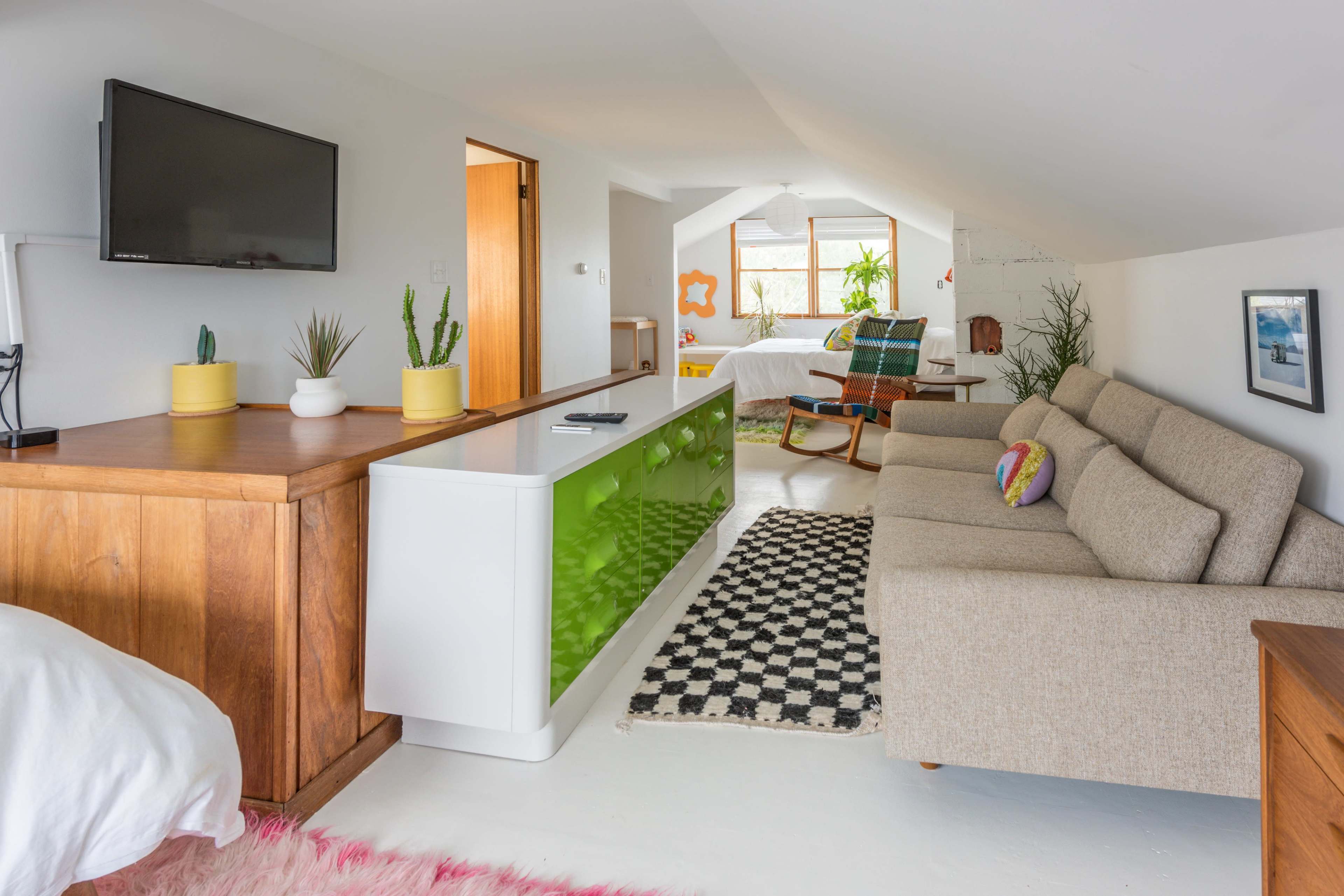 A light-filled, modern living space featuring a beige sofa, a green accent cabinet, and various plants decoratively arranged.