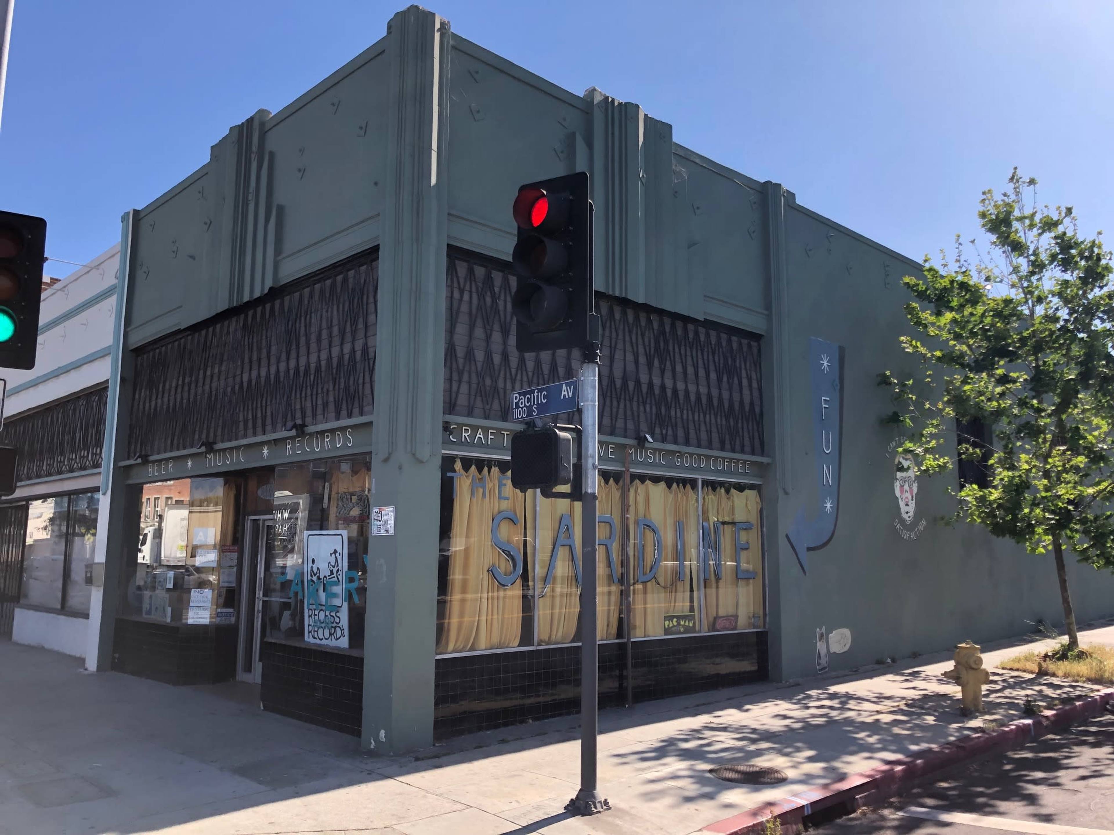 A green corner building with large windows featuring the sign "Sardine," which advertises craft beer, music, and coffee.