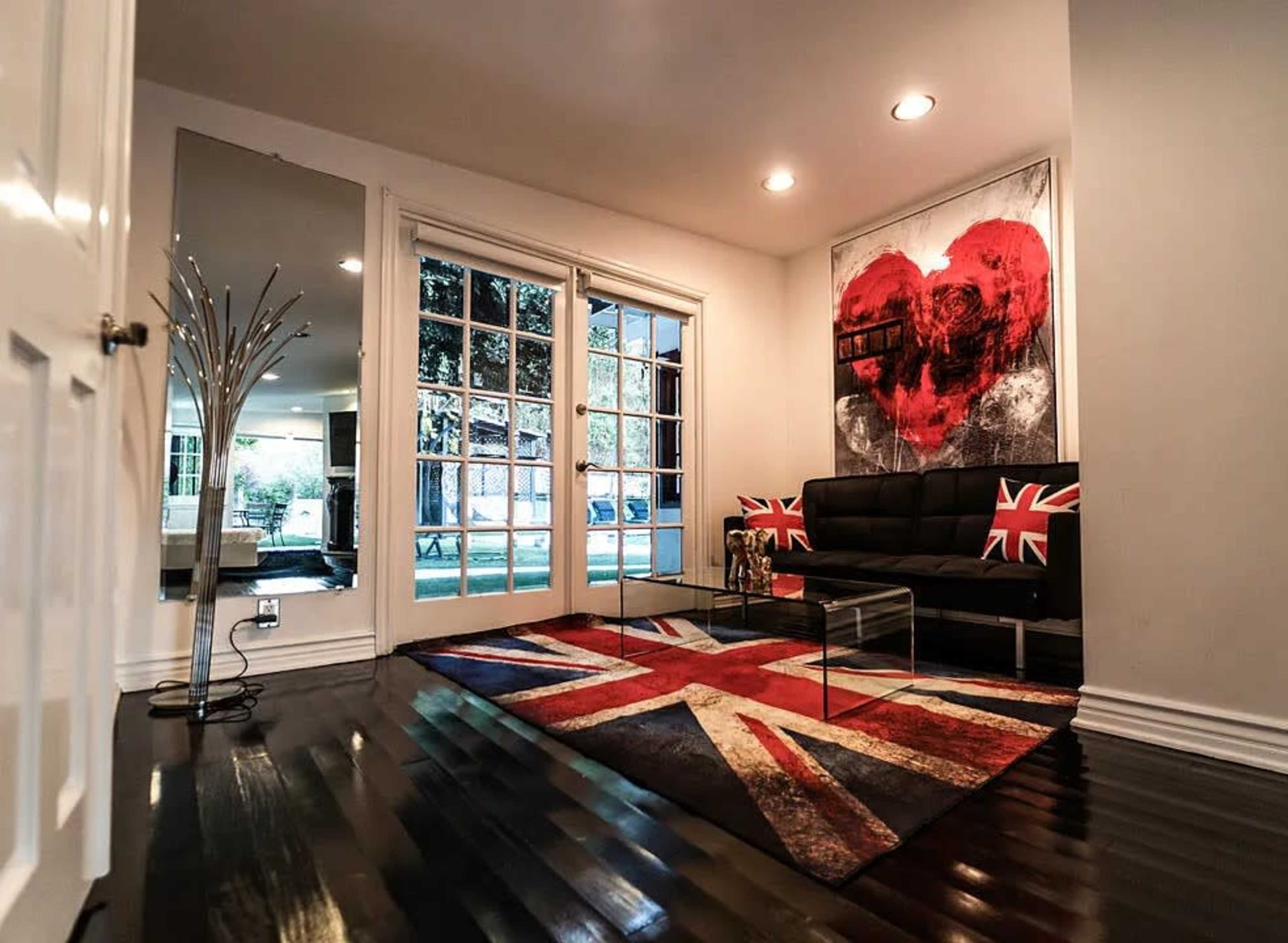 The image shows a modern living room with a black sofa, a glass coffee table, and a large wall art piece featuring a red heart, all on a Union Jack patterned rug.