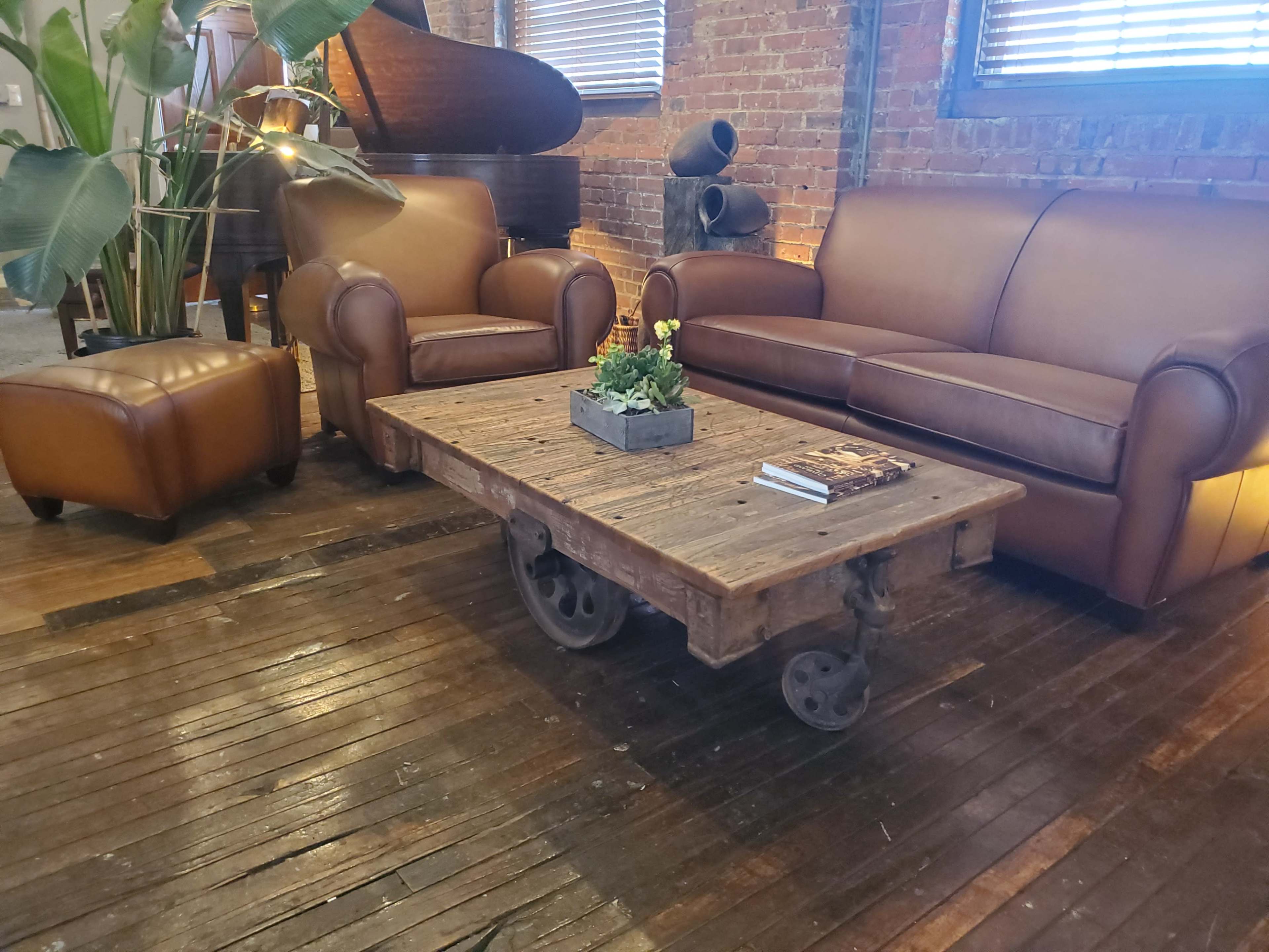 A seating area features a brown leather sofa and armchair, accompanied by a wooden coffee table on wheels, set on a hardwood floor.