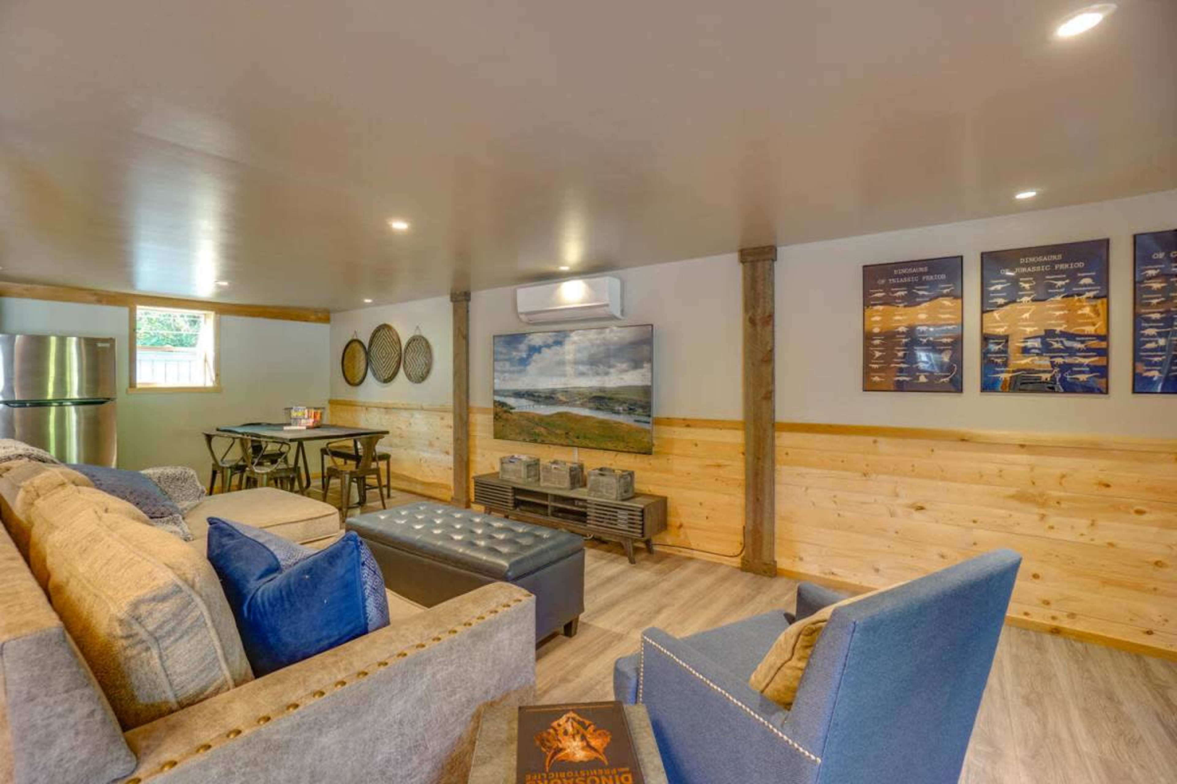 A modern, open living space featuring a sectional sofa, a coffee table, a television, and a dining area with two chairs and a table.