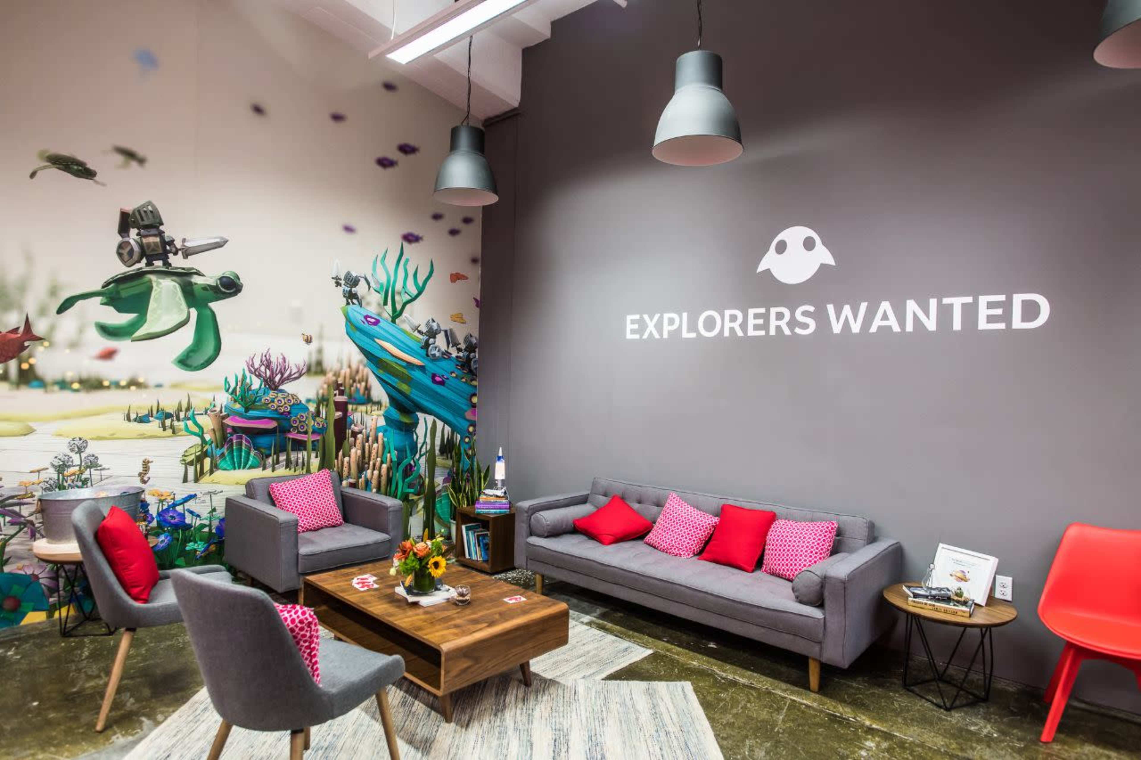 A modern lounge area with grey sofas, pink cushions, a wooden coffee table, and a colorful mural featuring underwater scenes on the wall.