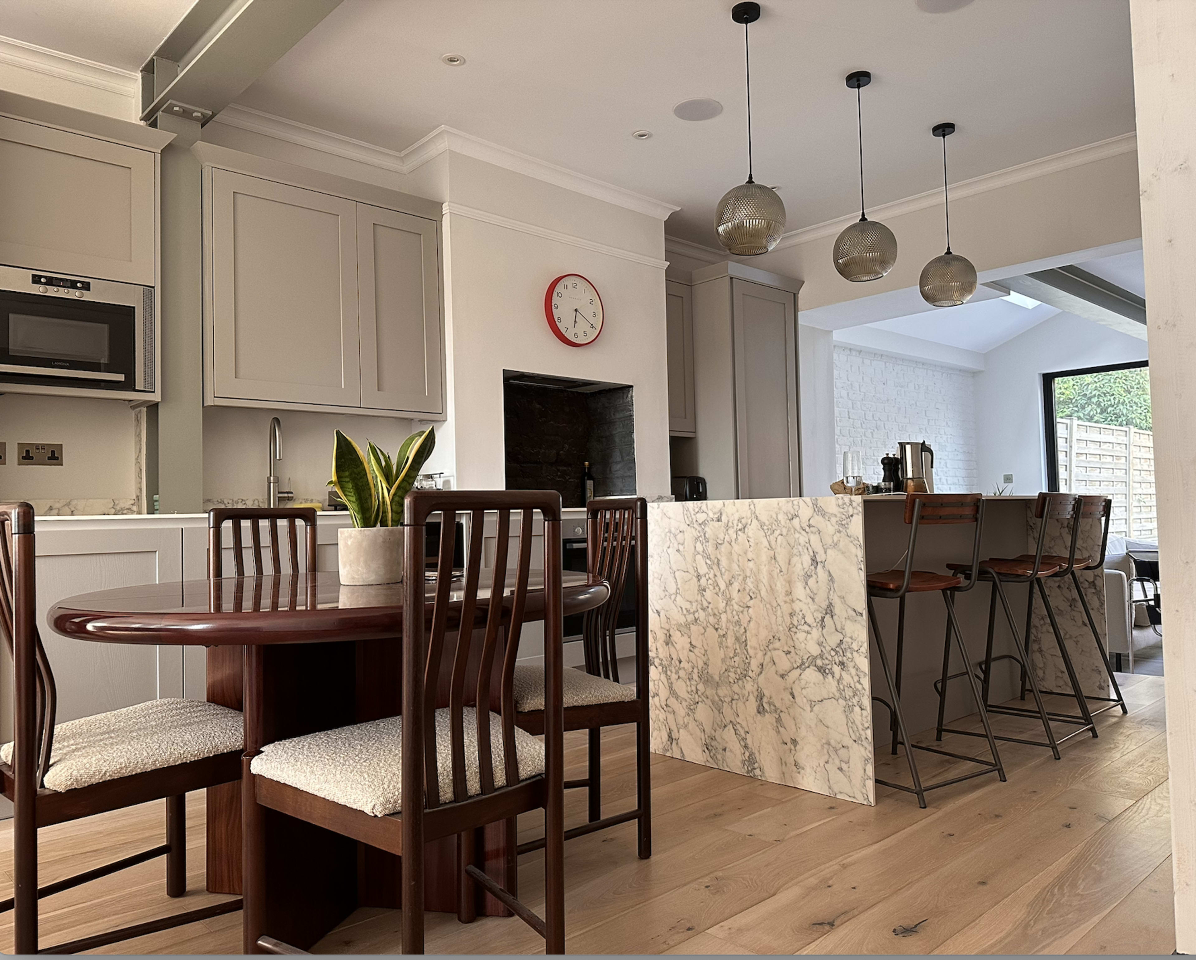 A modern kitchen features a marble island with high stools, a round dining table, and pendant lighting.