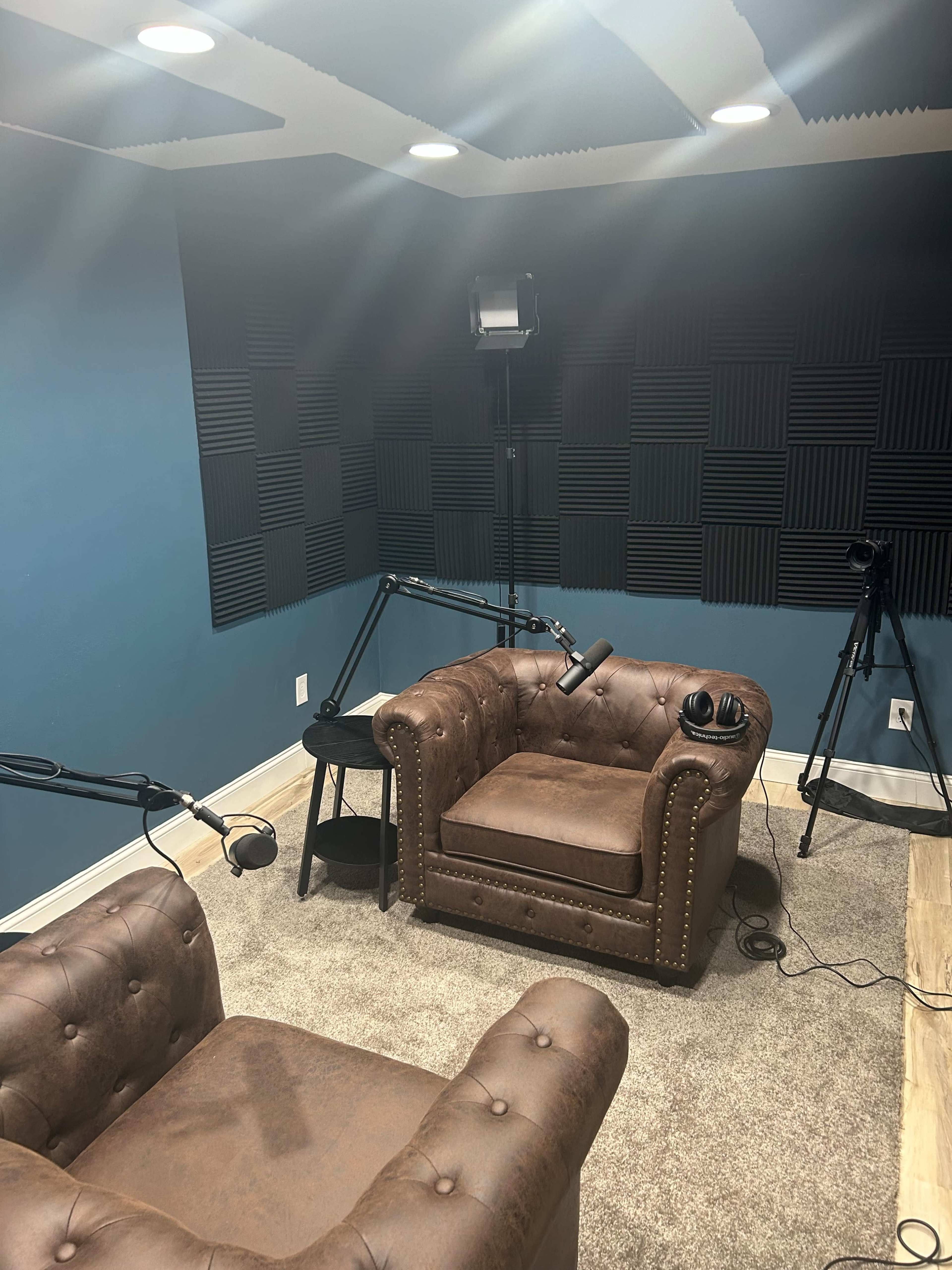The image shows a soundproofed room with two brown leather chairs, a small table, and equipment for recording or broadcasting.