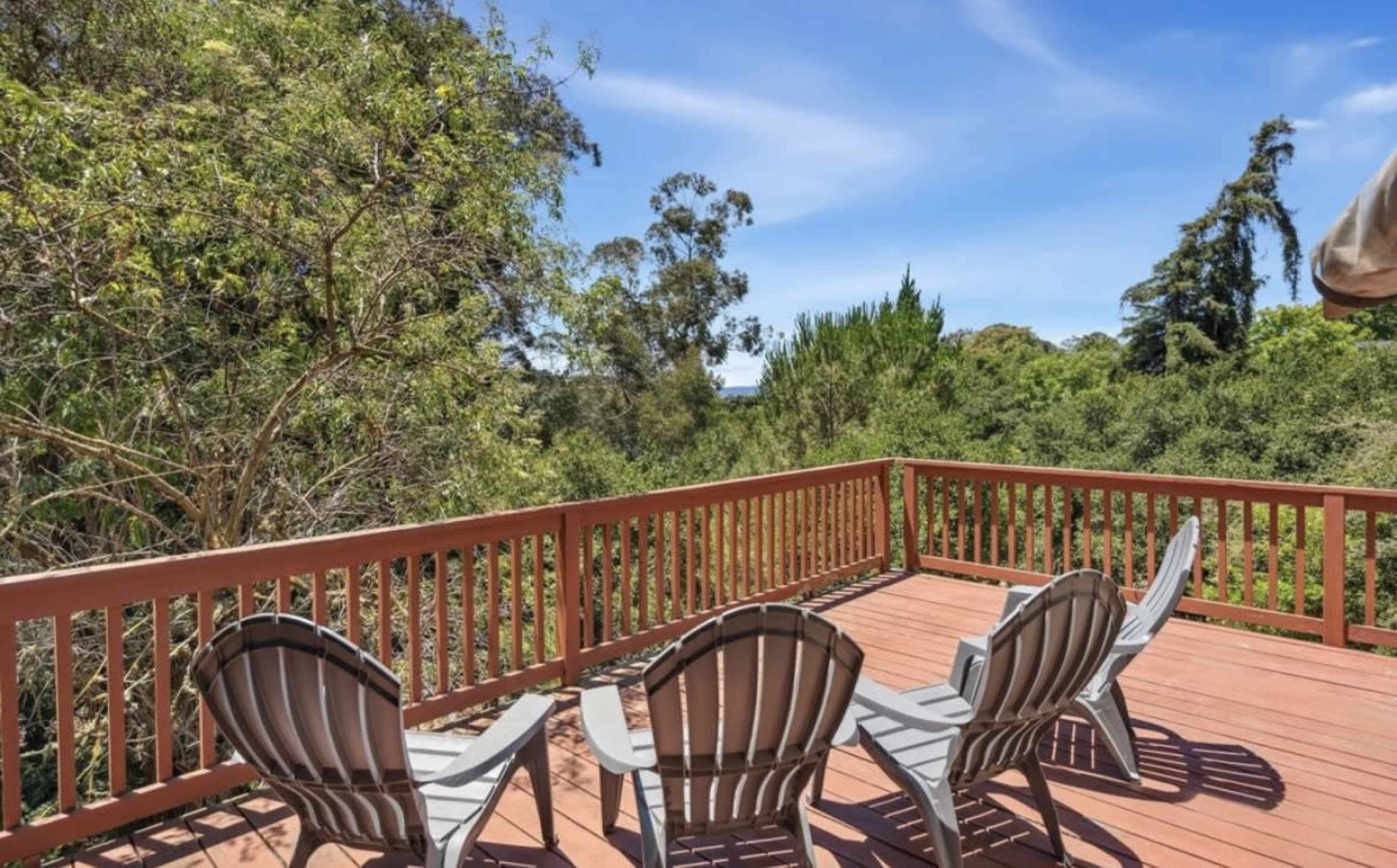 A deck with wooden railing features several gray chairs overlooking a lush, green landscape.