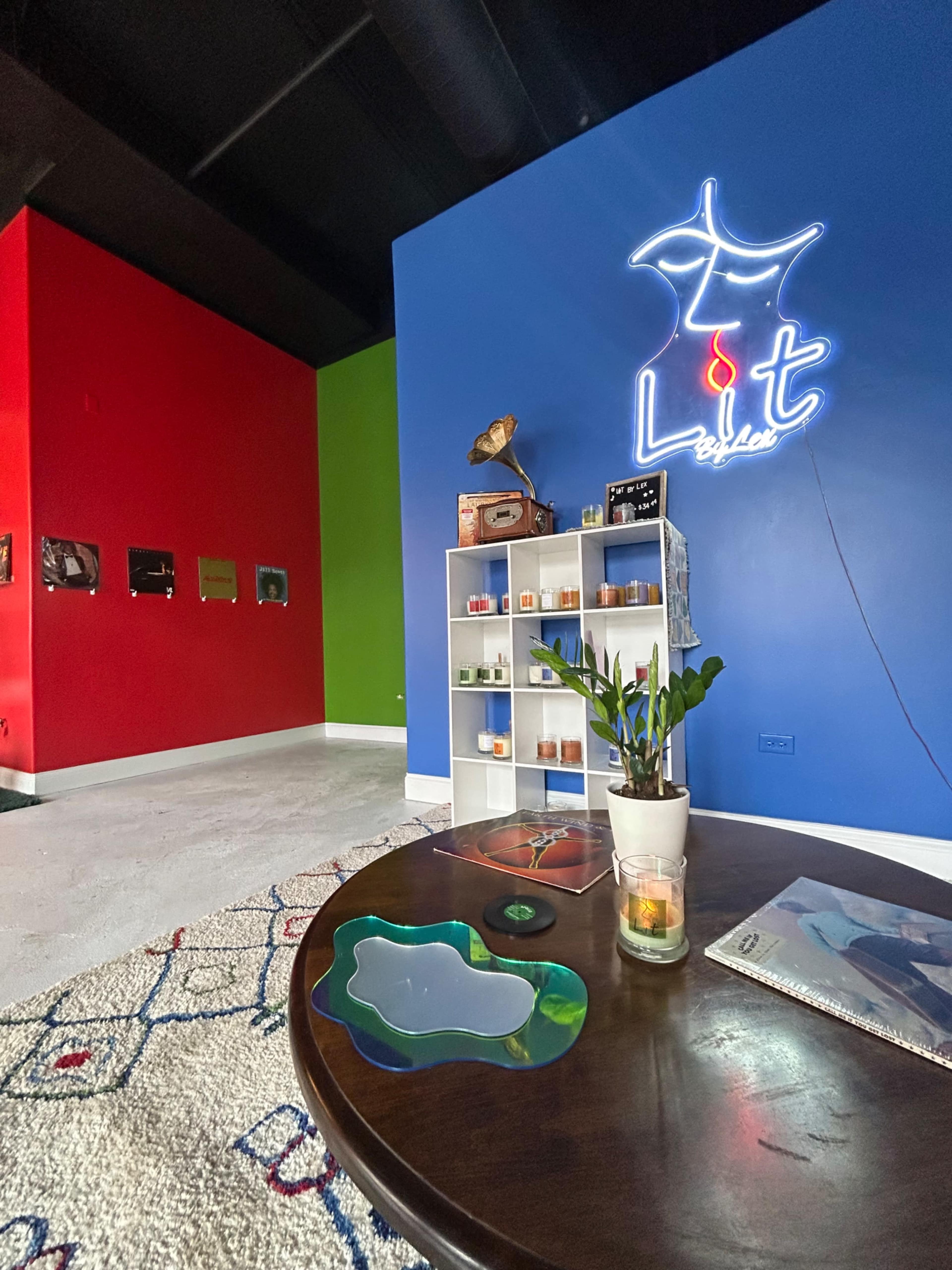 A colorful room with red, green, and blue walls, featuring a white shelving unit filled with candles and a small plant on a wooden table.