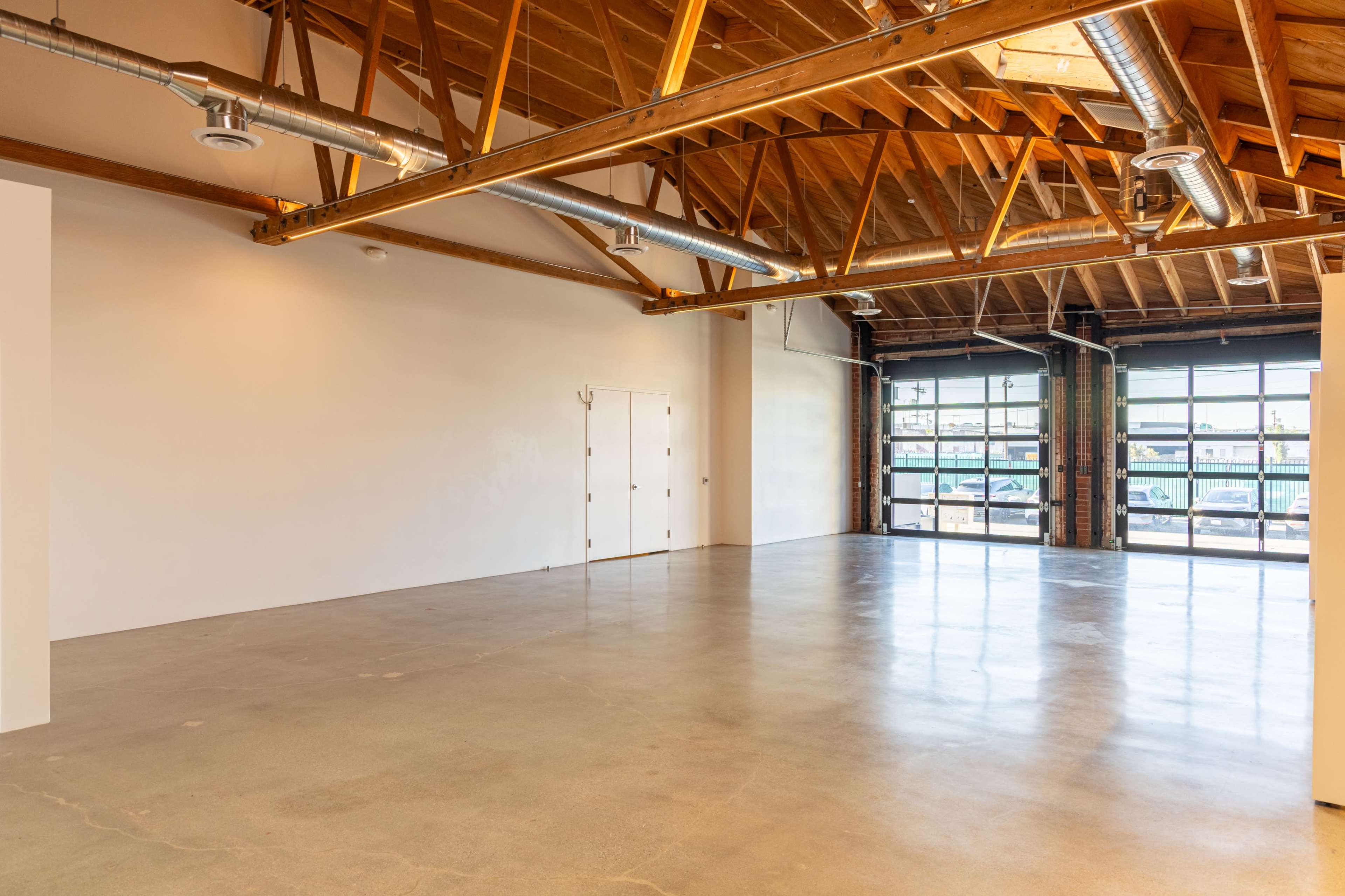 The image shows an empty industrial-style space with wooden beams and large windows along one side.