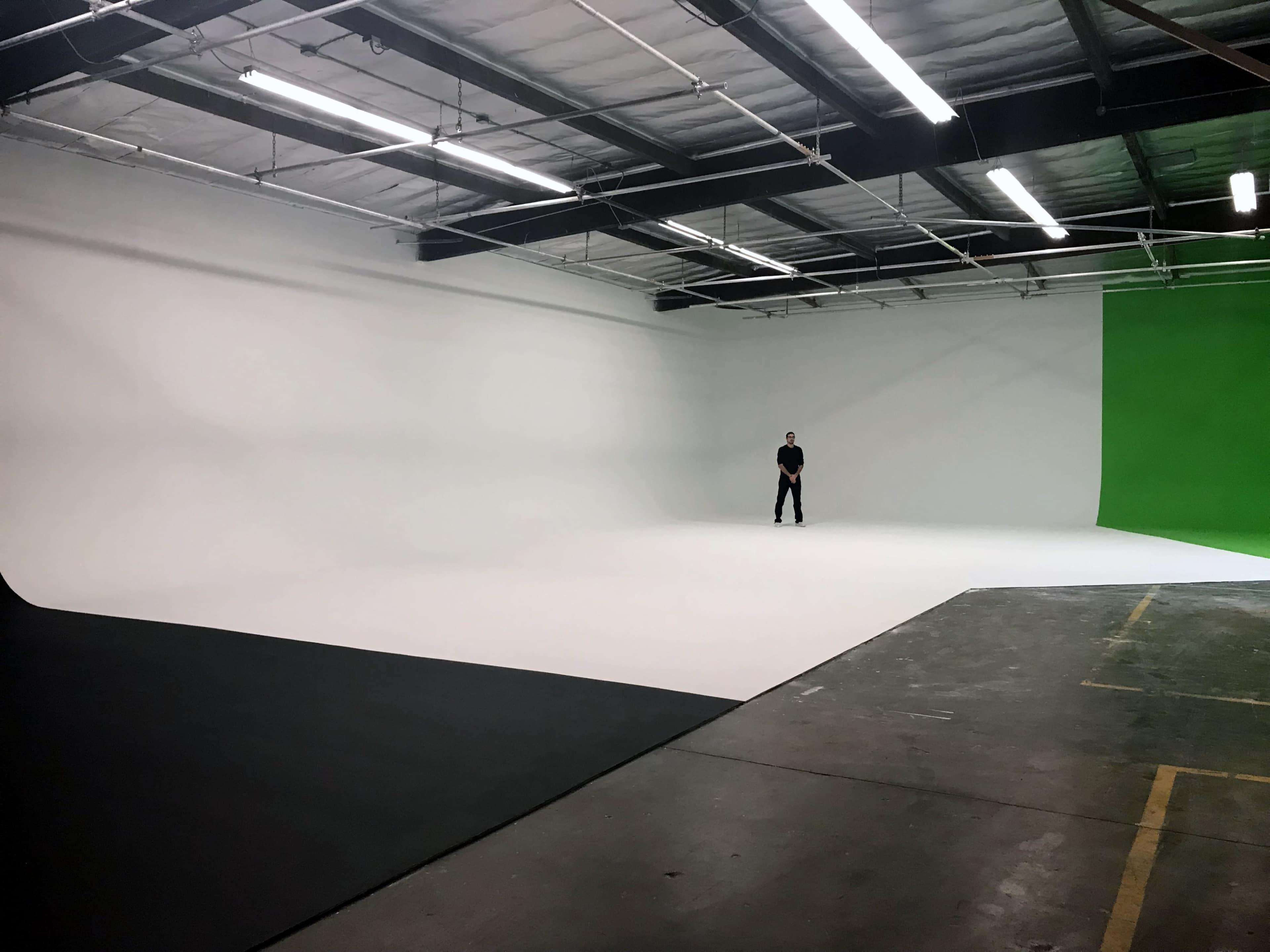 A large photography studio with a person standing in the center, surrounded by a white backdrop and a green screen.