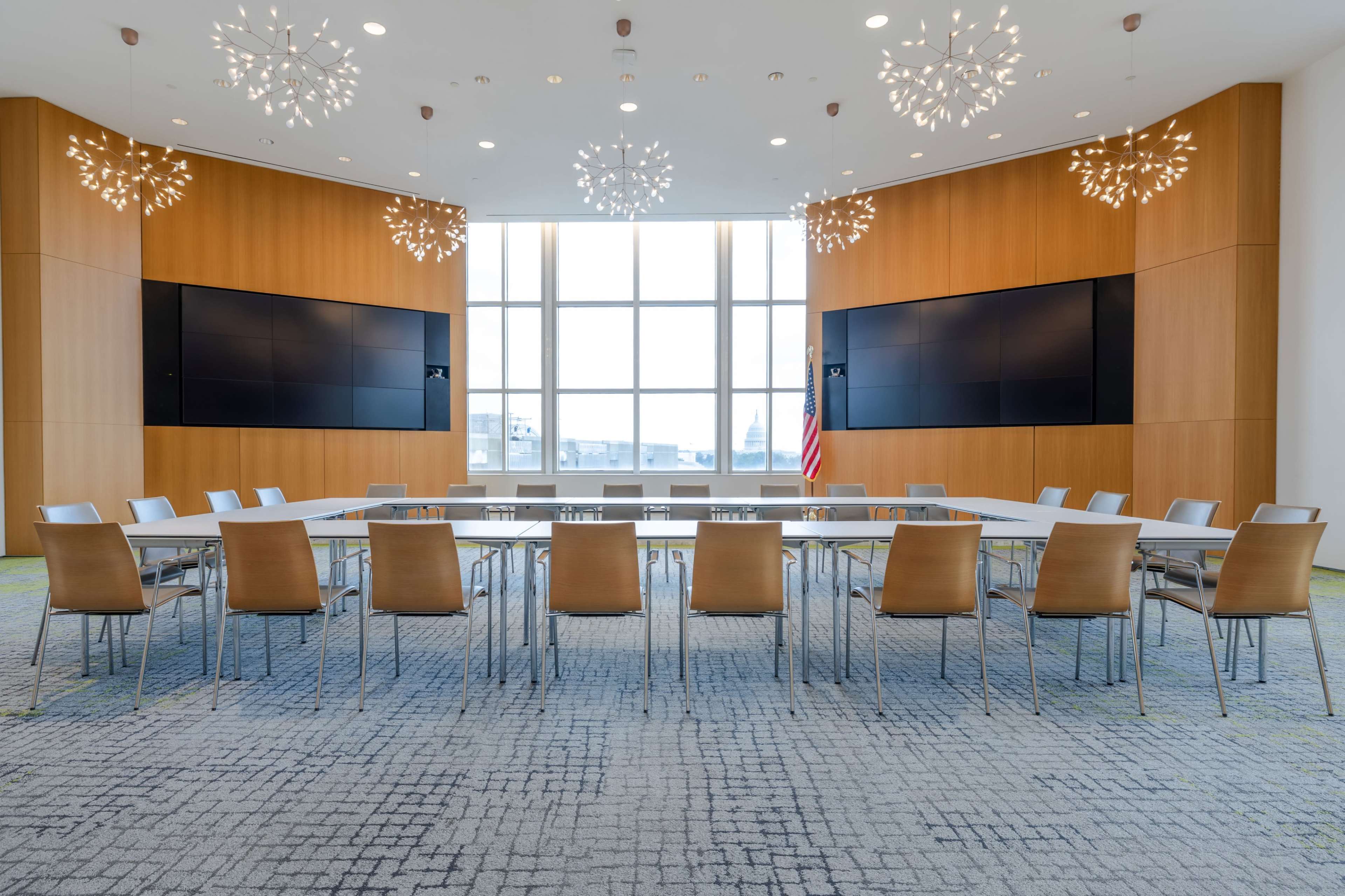 A modern conference room features a long table surrounded by chairs, with large screens mounted on wooden walls and decorative light fixtures.