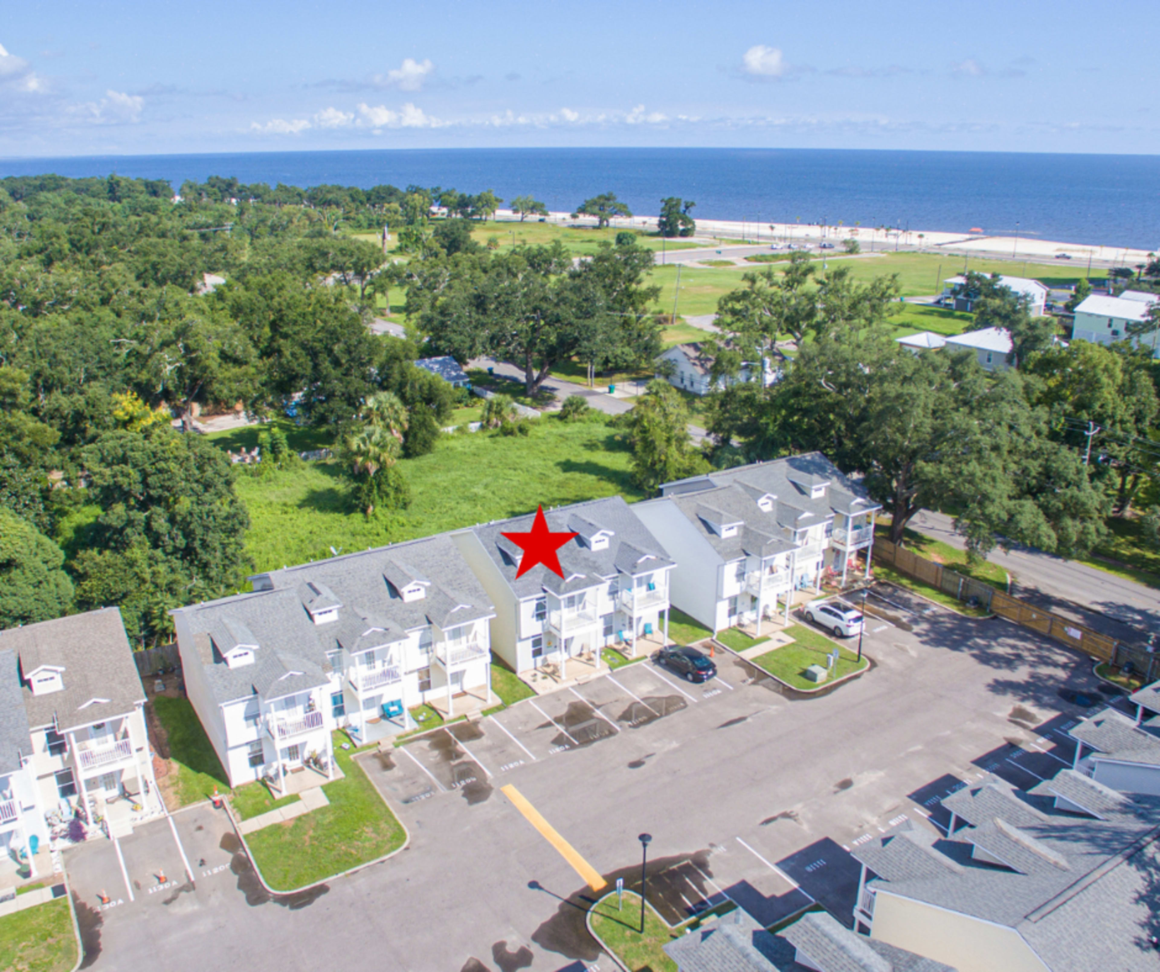 A row of residential buildings with a marked unit near a beach and open green space in the background.