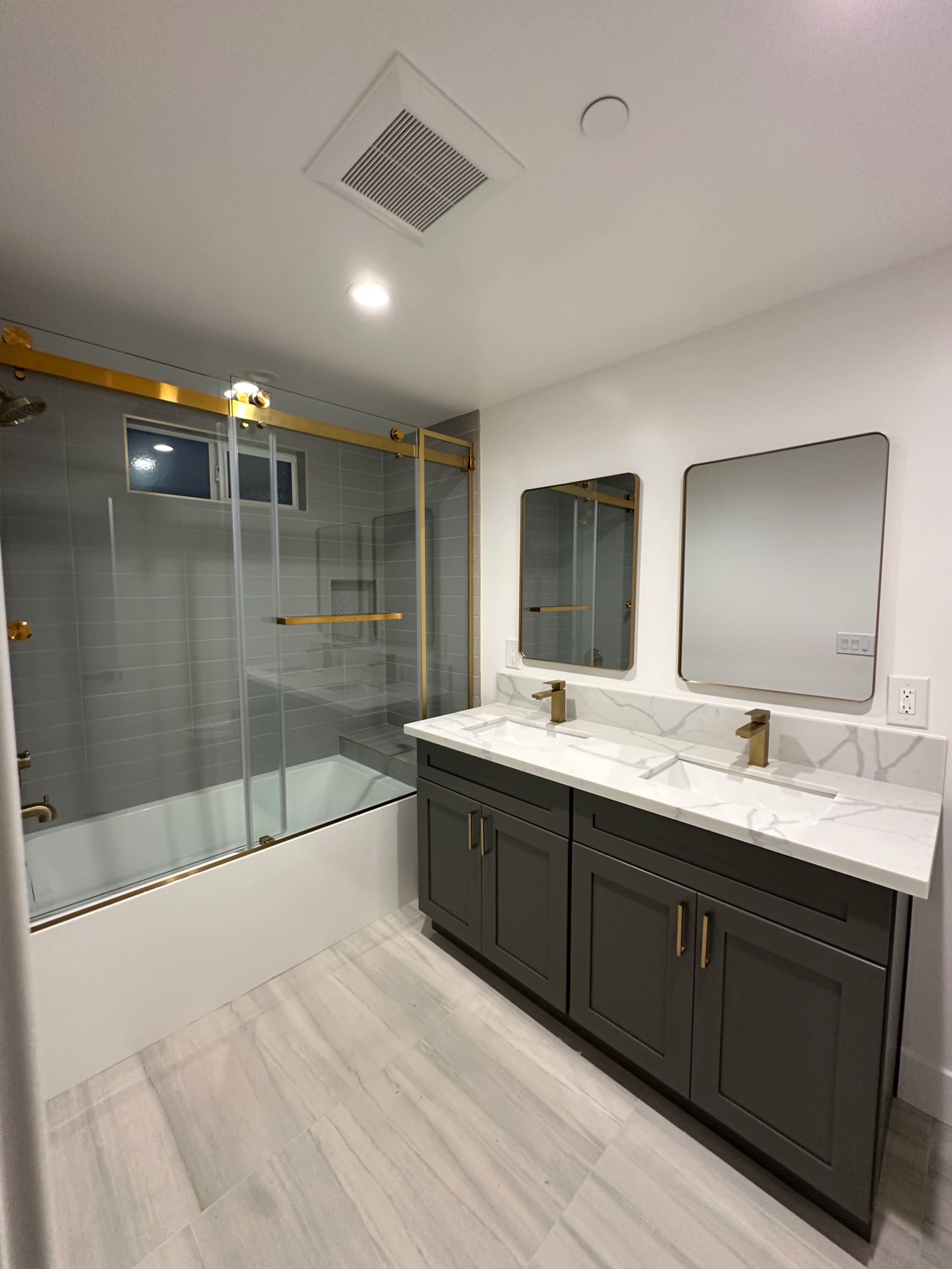 The image shows a modern bathroom featuring a glass shower enclosure, dual mirrors above a marble countertop, and dark cabinetry beneath the sink.