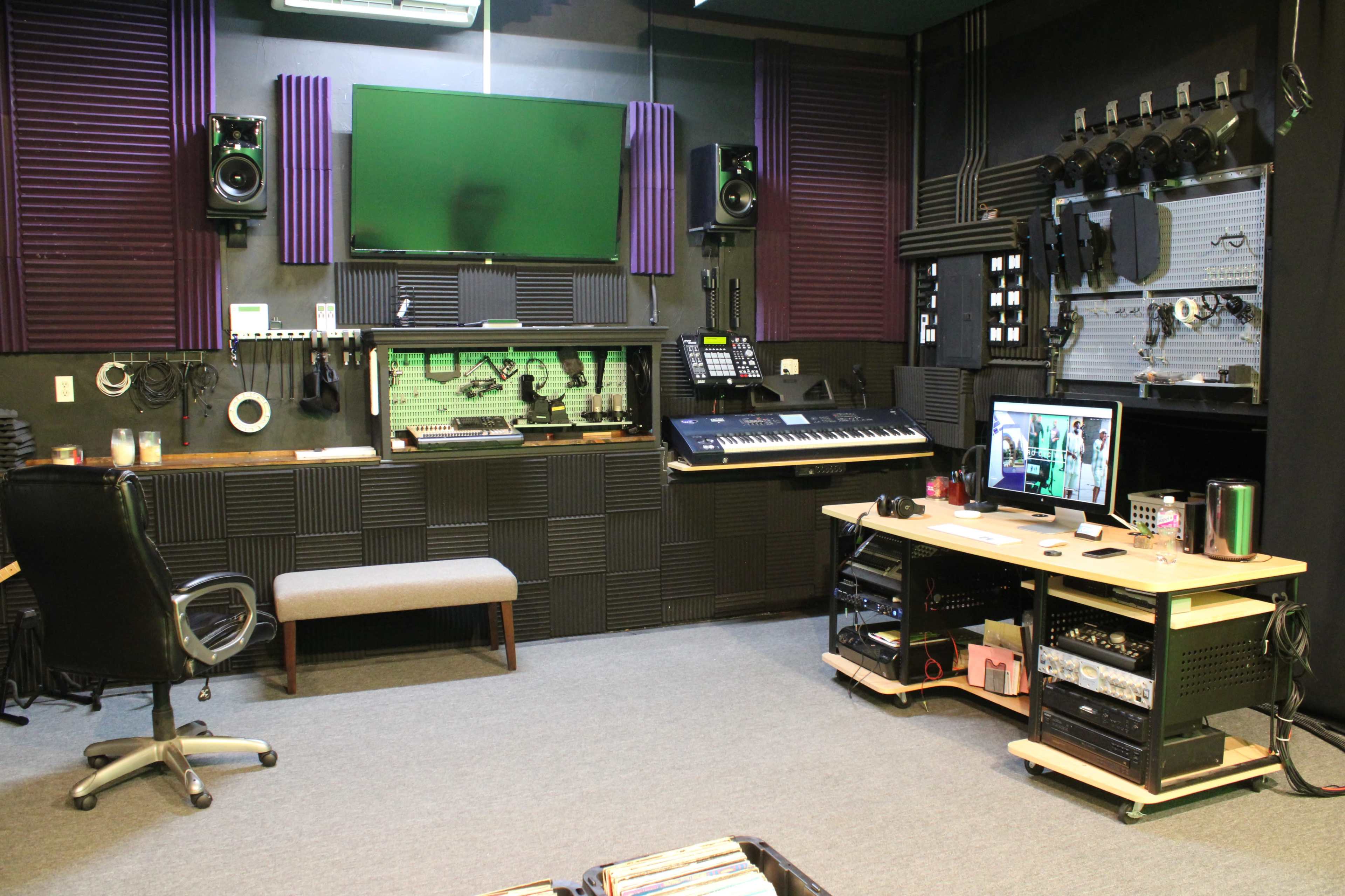 A recording studio with soundproofing panels, a keyboard, an audio mixer, a computer setup, and various music equipment arranged neatly on a carpeted floor.