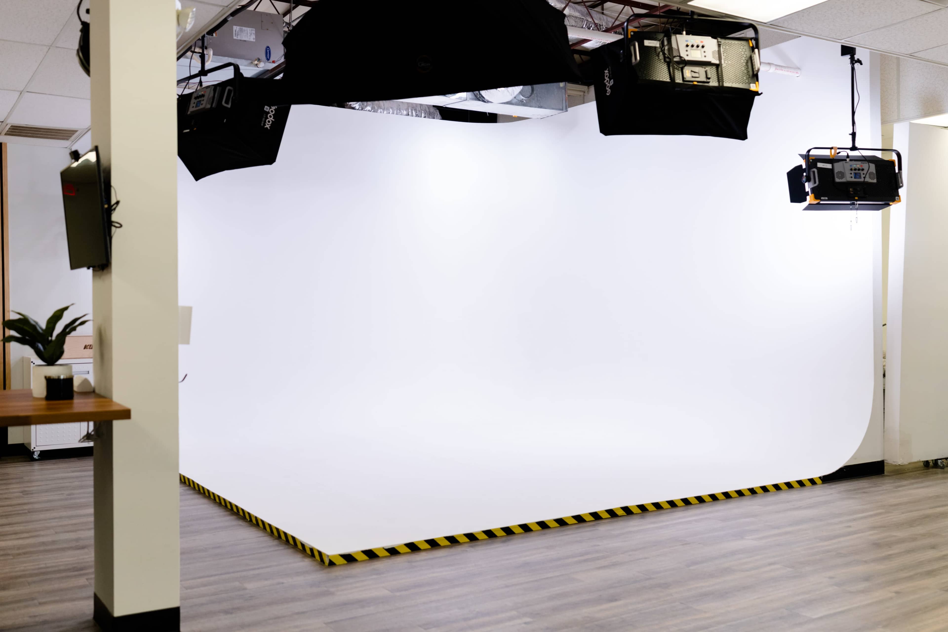 A blank studio space with a white backdrop and overhead lighting, complemented by a striped safety border on the floor.