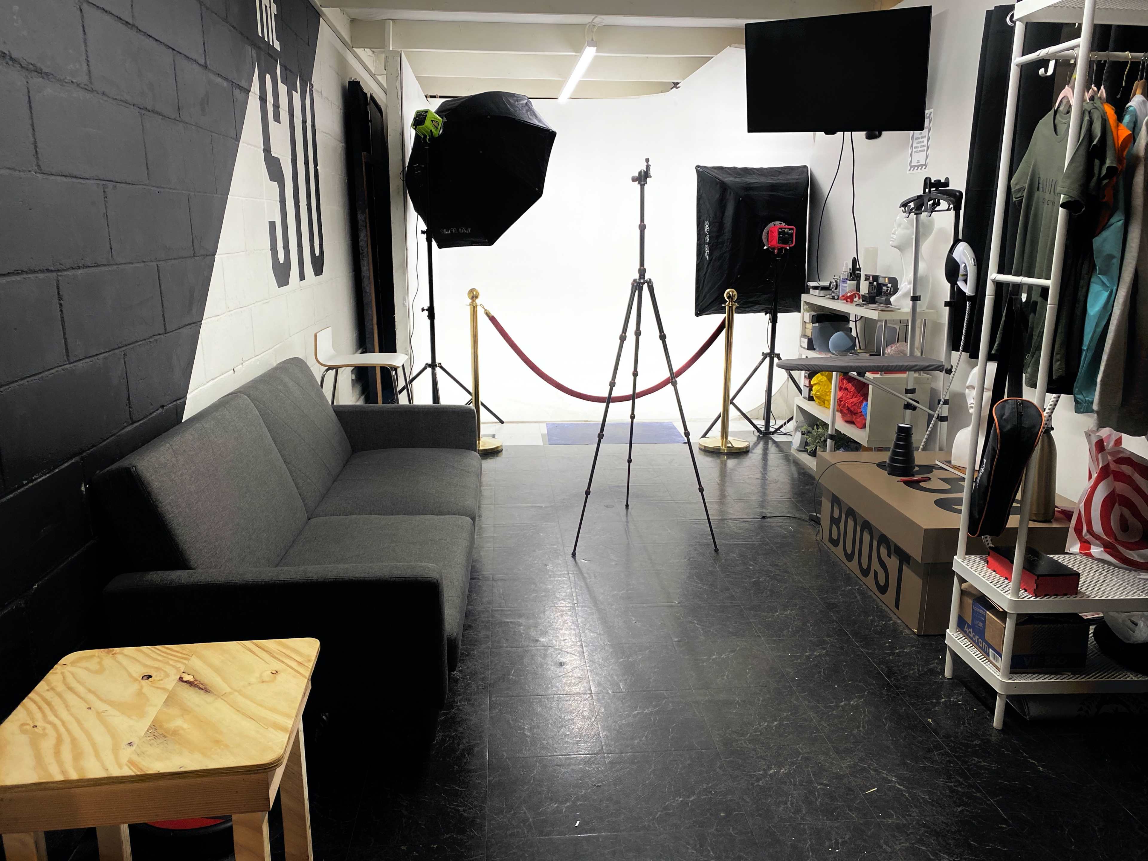 A photo studio featuring a gray sofa, a wooden table, photography equipment, and a backdrop.
