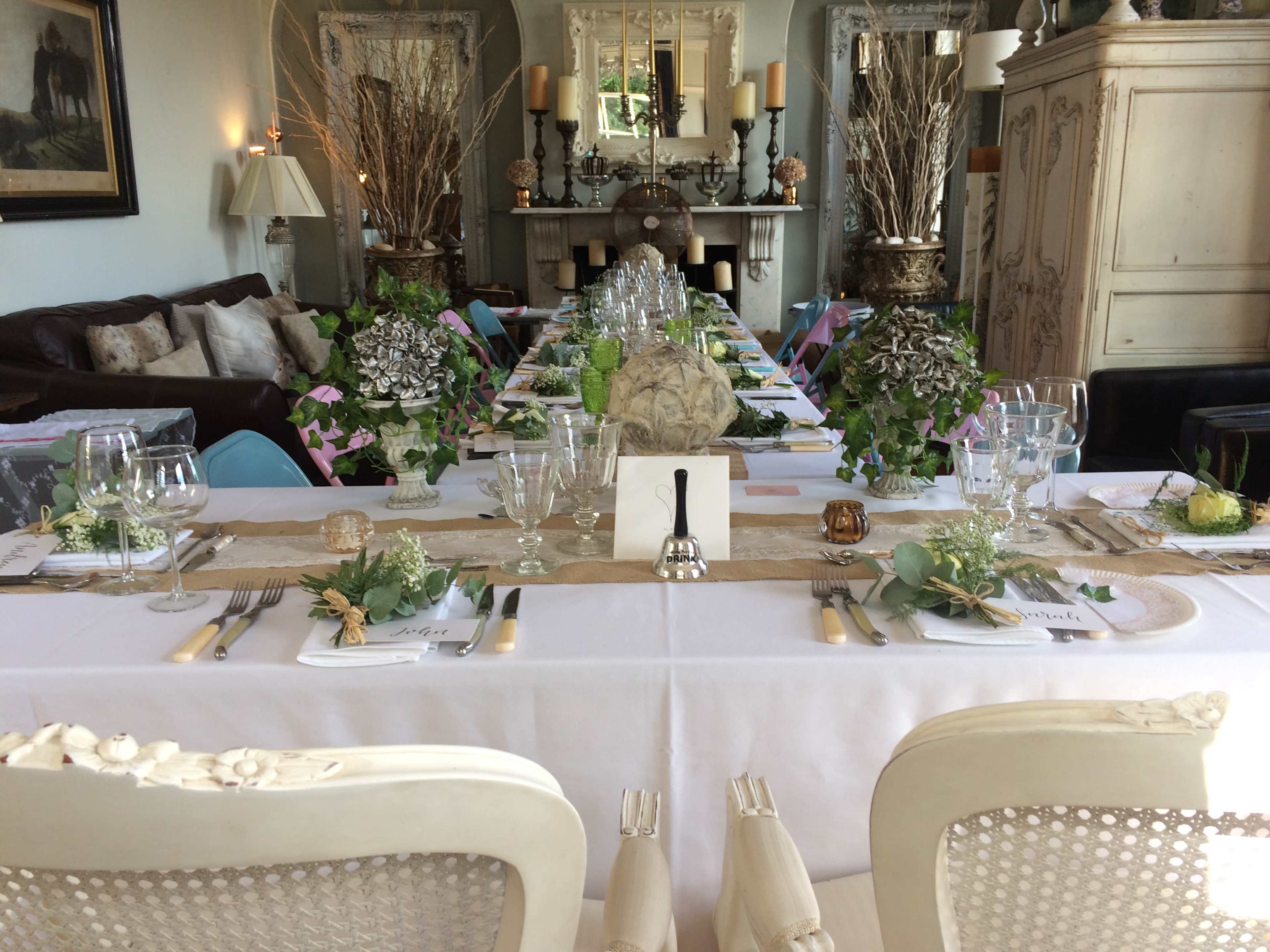 A long dining table is elegantly set with glassware, cutlery, and floral centerpieces in a well-decorated room.