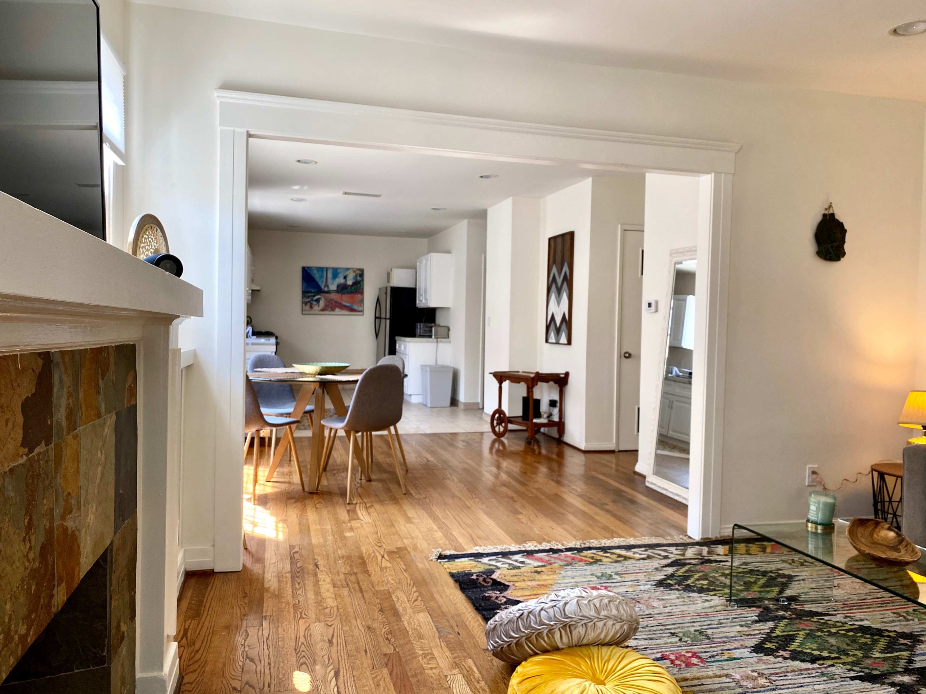 A modern interior space with hardwood floors, a patterned rug, a small dining area, and a view into an adjacent room containing a kitchen and living area.