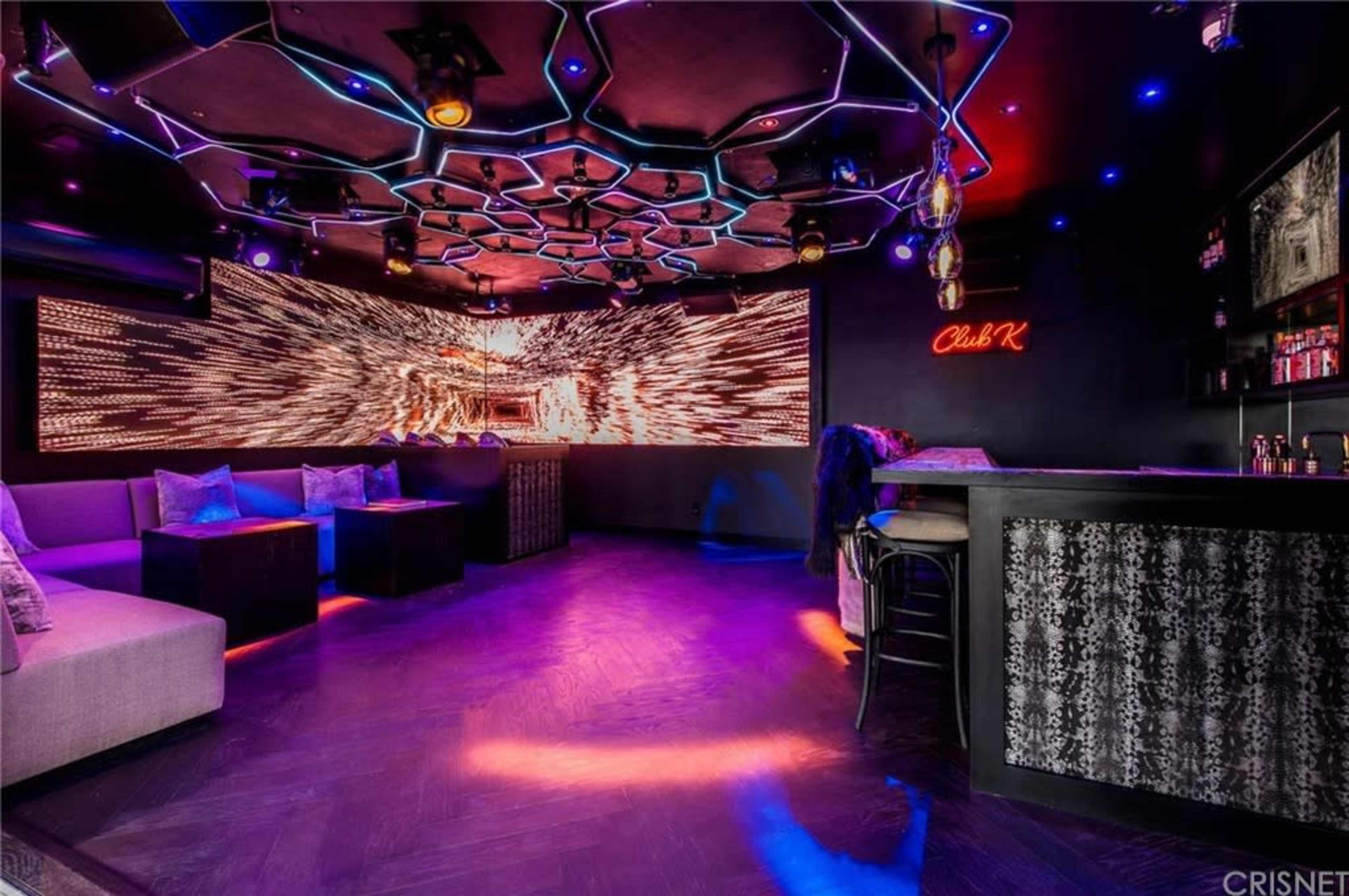 A modern lounge area with hexagonal ceiling designs and vibrant lights, featuring a bar counter and seating.