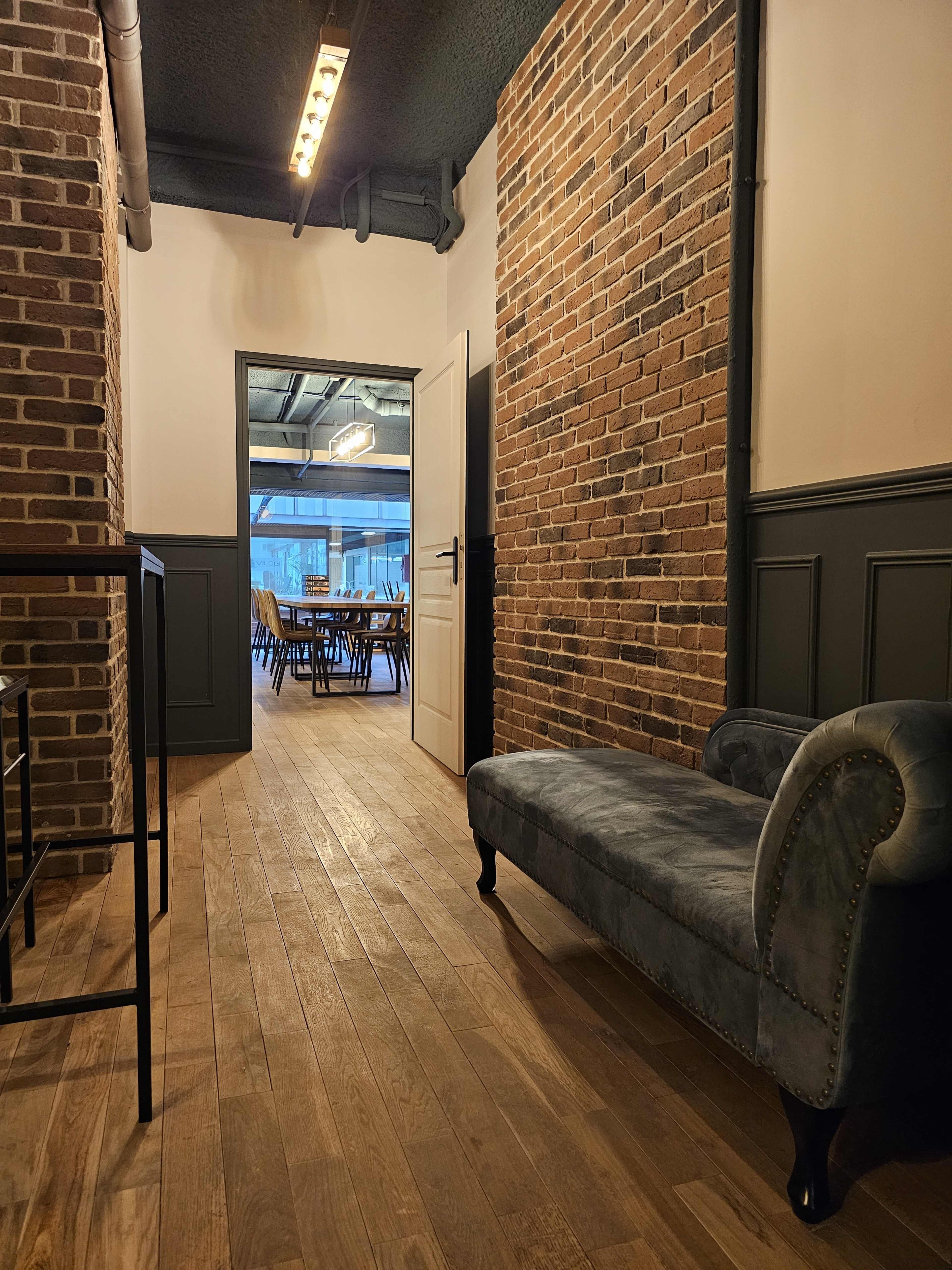 A narrow hallway features exposed brick walls, wooden flooring, and a velvet bench, leading to a dining area visible through an open door.