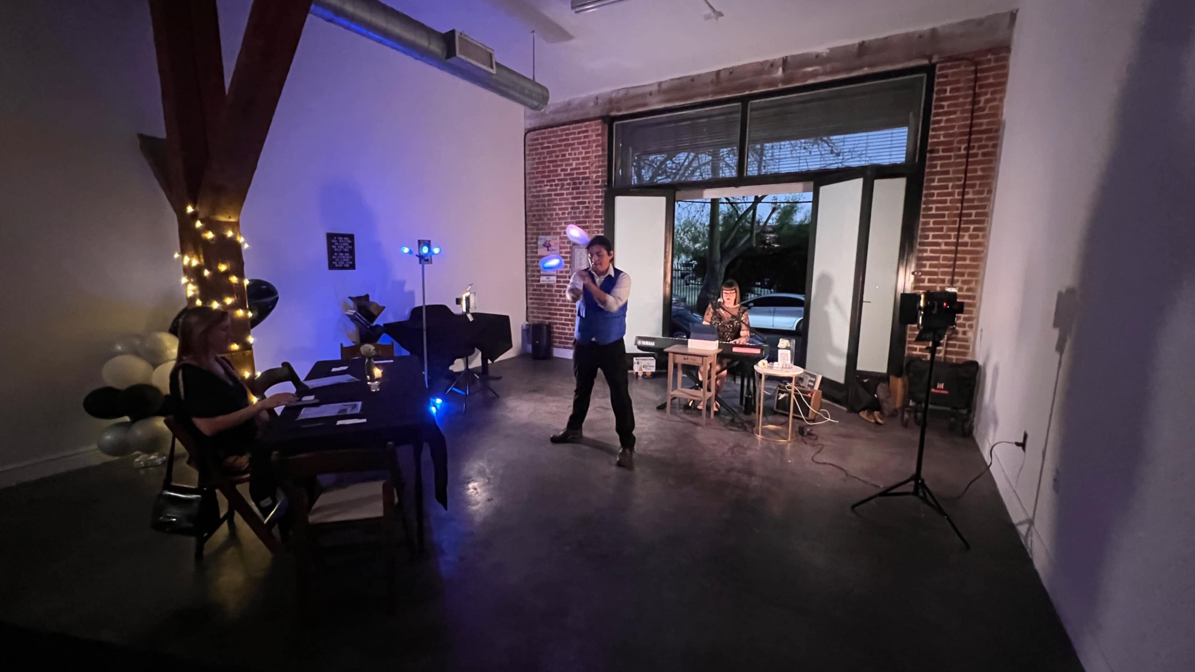 A performer is juggling in a modern, sparsely furnished room with brick walls and large windows.