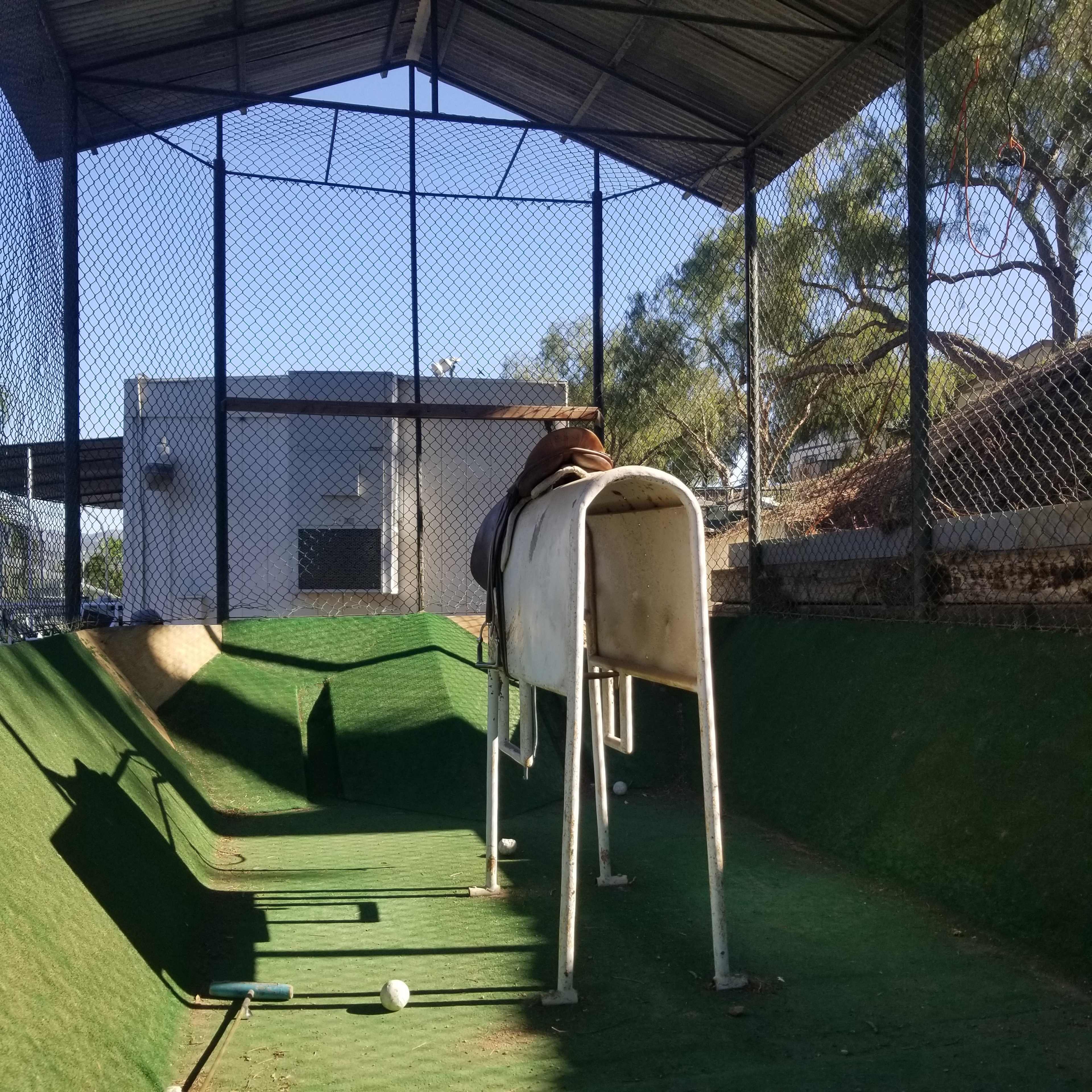 A batting cage with a horse dummy positioned on a raised platform in a fenced enclosure.