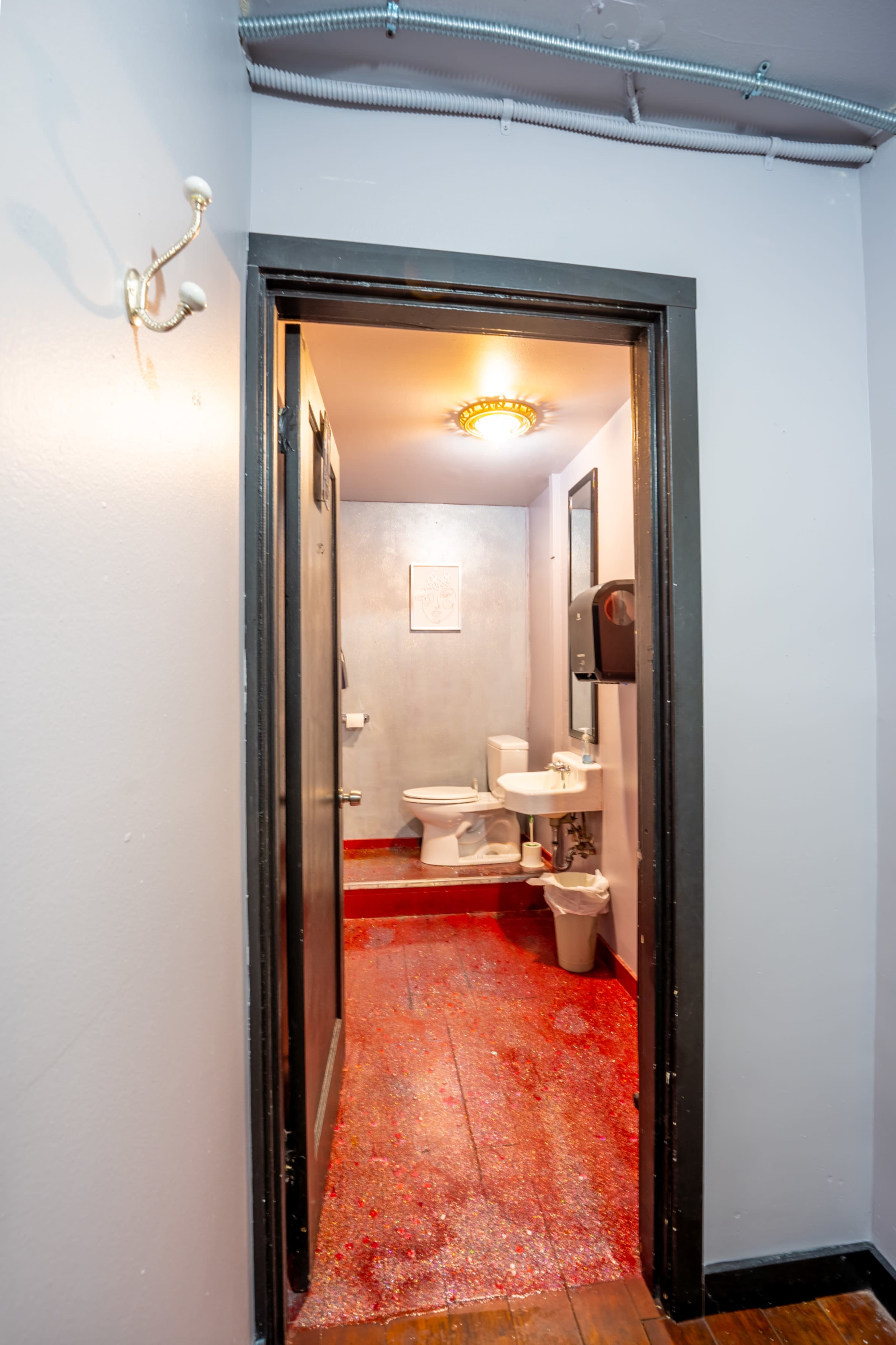 A small bathroom is visible through an open door, featuring a toilet, sink, and red flooring.