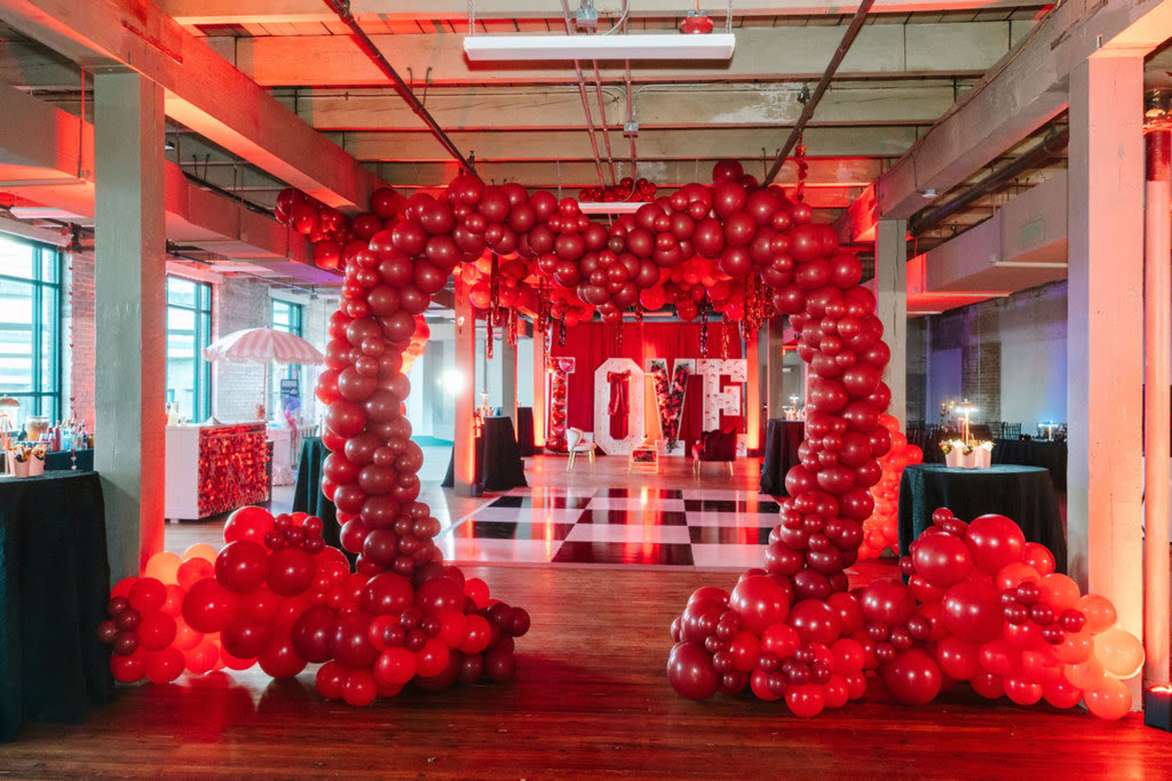 The image shows a decorated event space featuring a large balloon arch in red, with the letters "I O F" displayed inside the arch, and tables set up around a checkered dance floor.