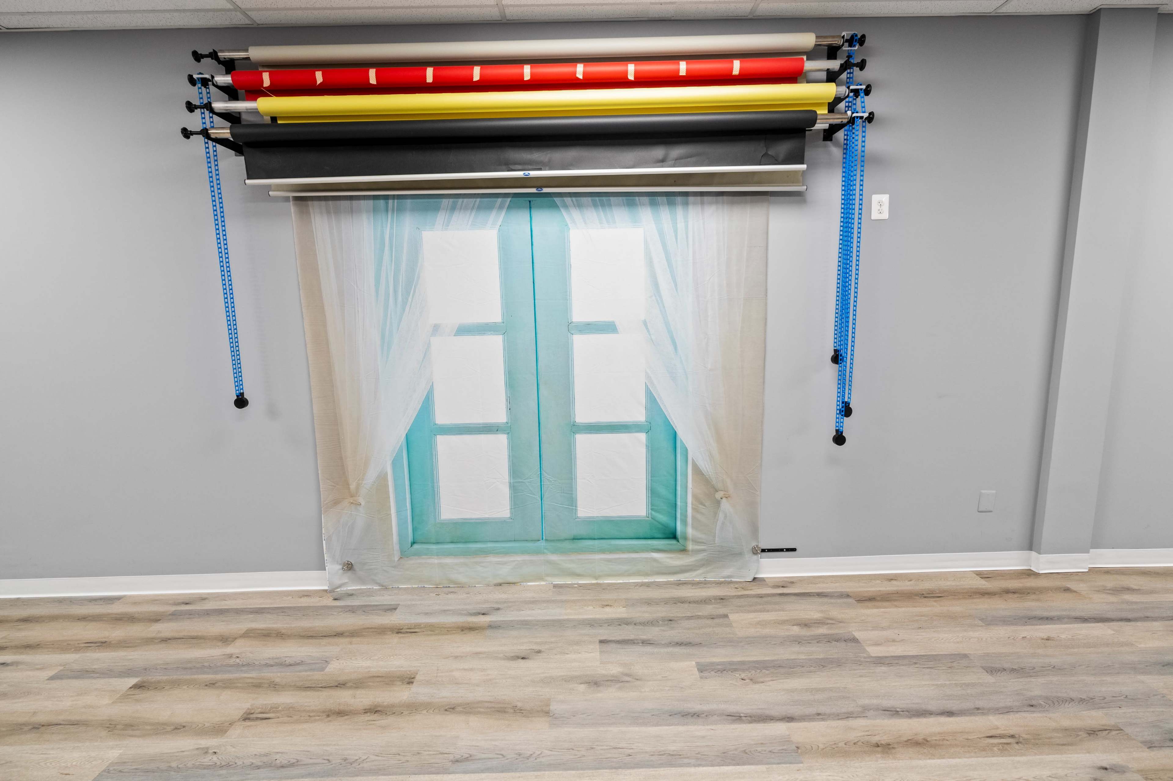 A backdrop setup features a window scene with curtains, complemented by colorful roller paper positioned above.