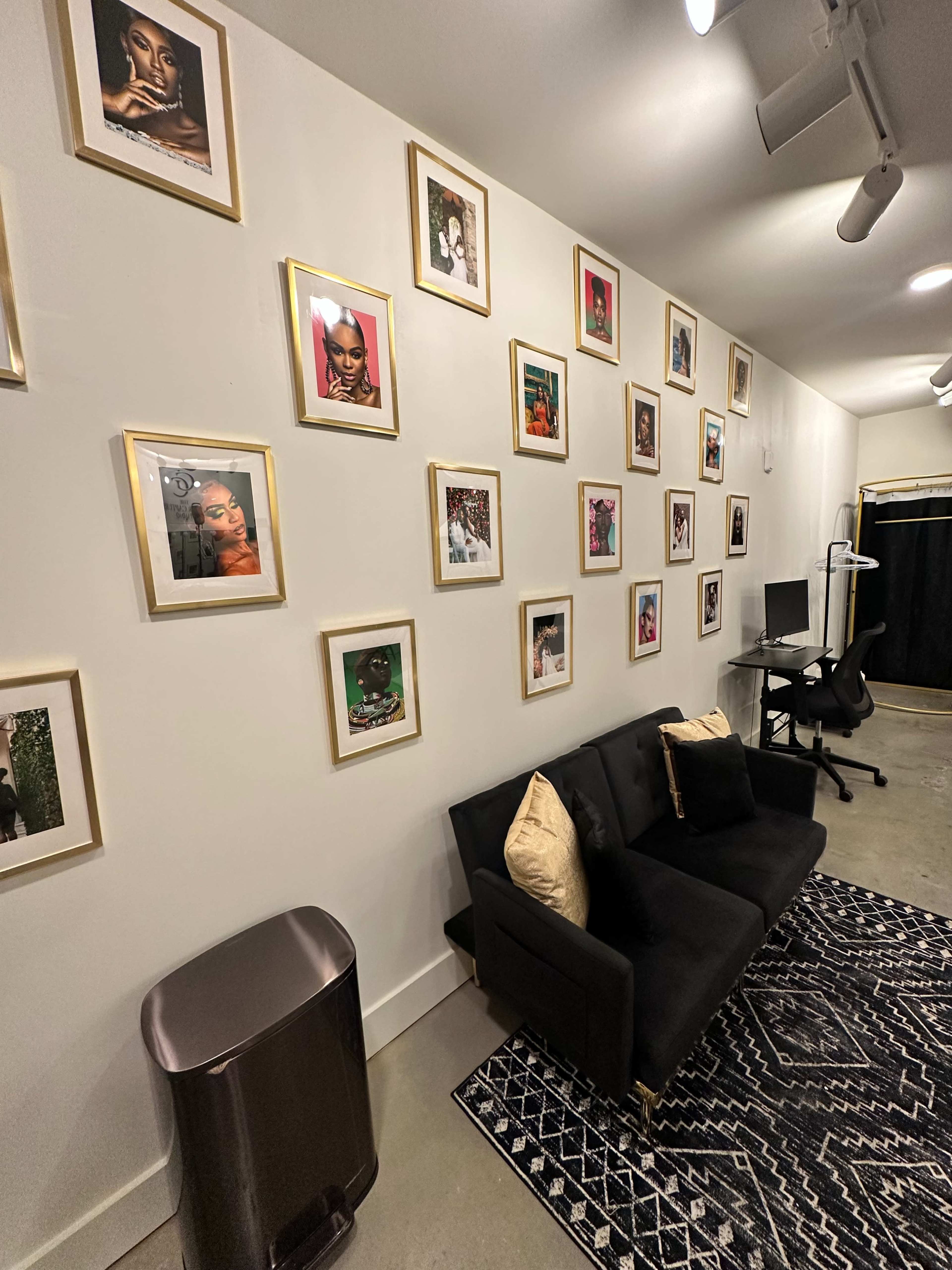 The image shows a modern interior space featuring a black couch, a patterned rug, and a wall adorned with framed photographs.