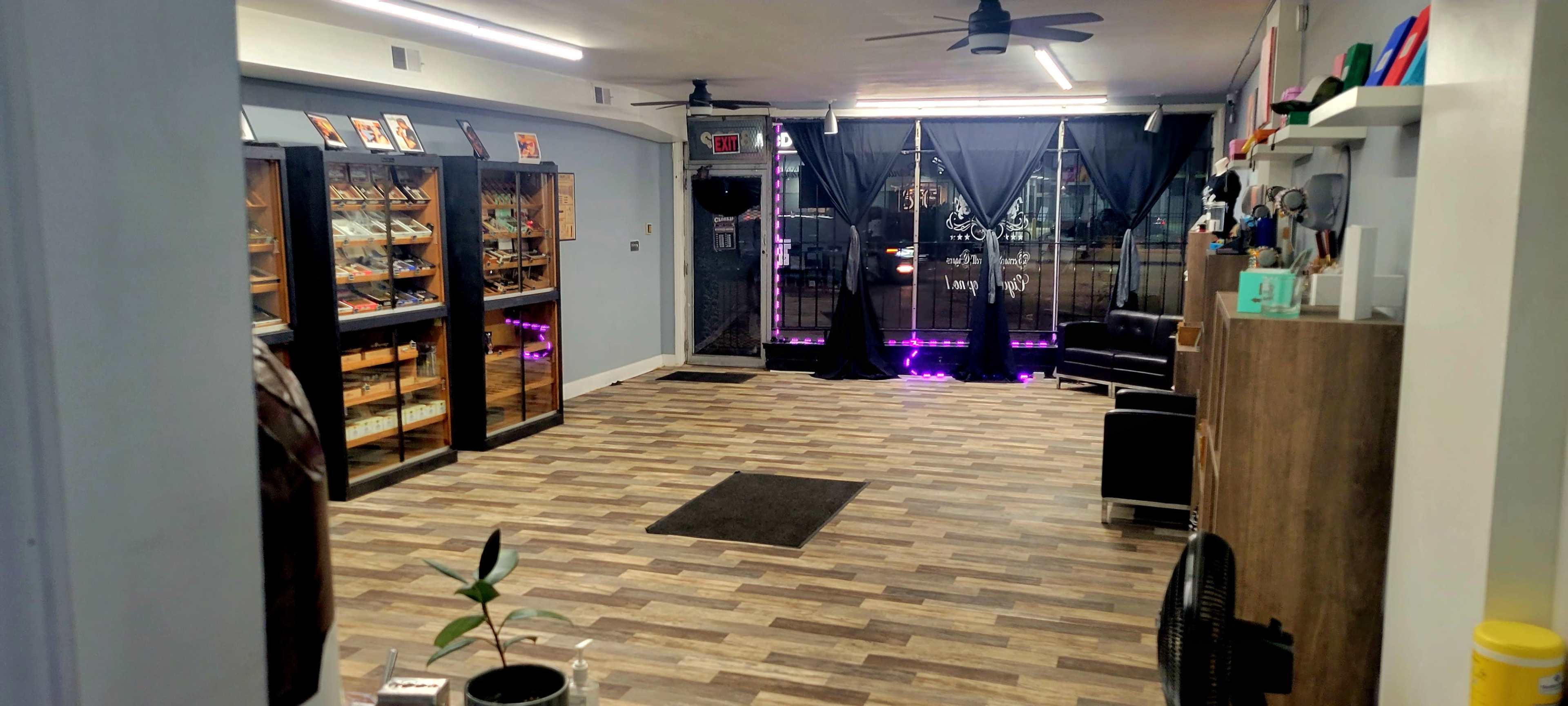 The image shows a retail space with a wooden floor, display cases along the walls, and seating near a glass entrance covered by black curtains.