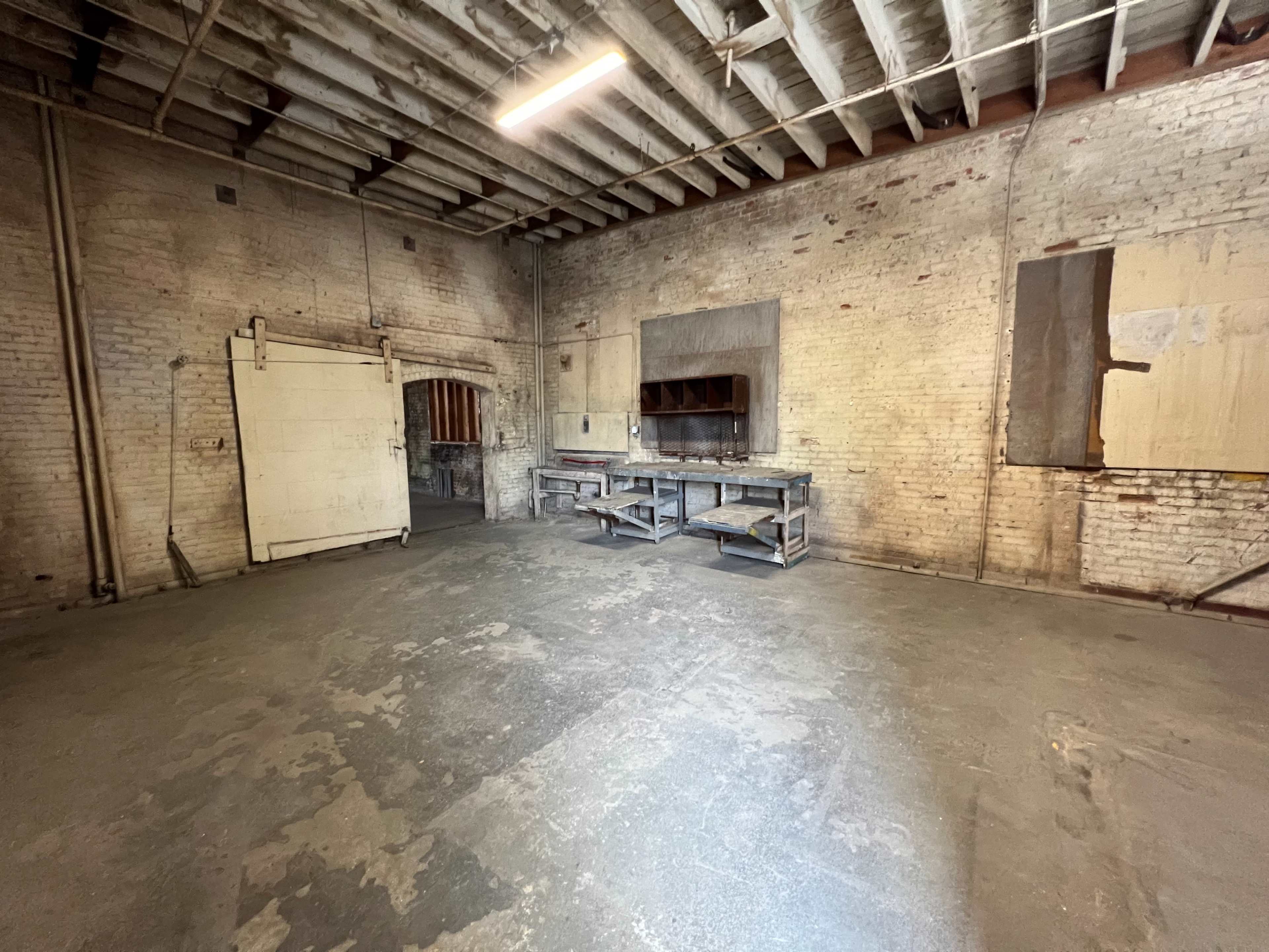 An empty room with exposed brick walls, wooden beams, and a workbench positioned against one wall.