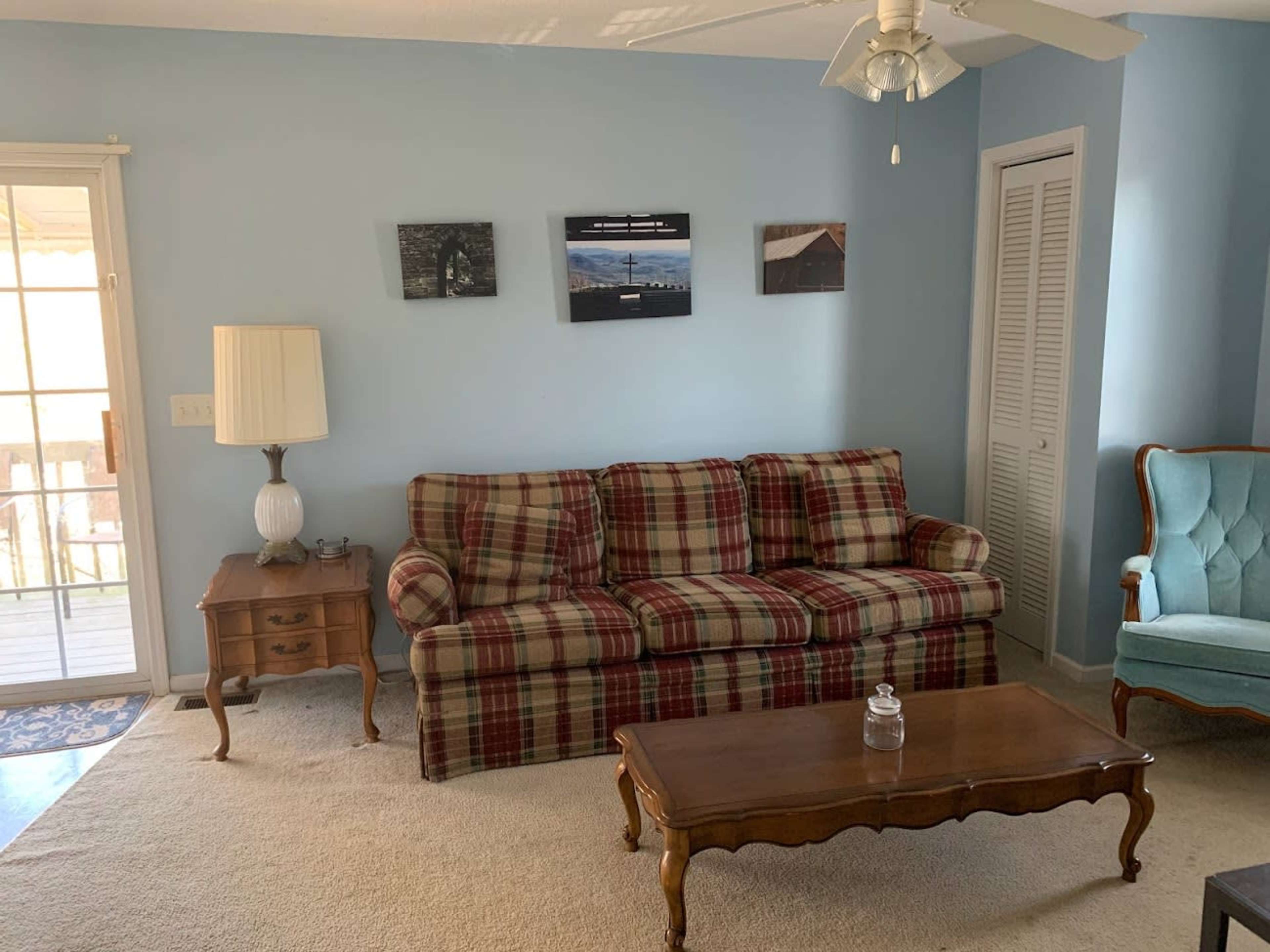 The living room features a plaid sofa, a wooden coffee table, and a lamp next to a door leading to an outdoor space.