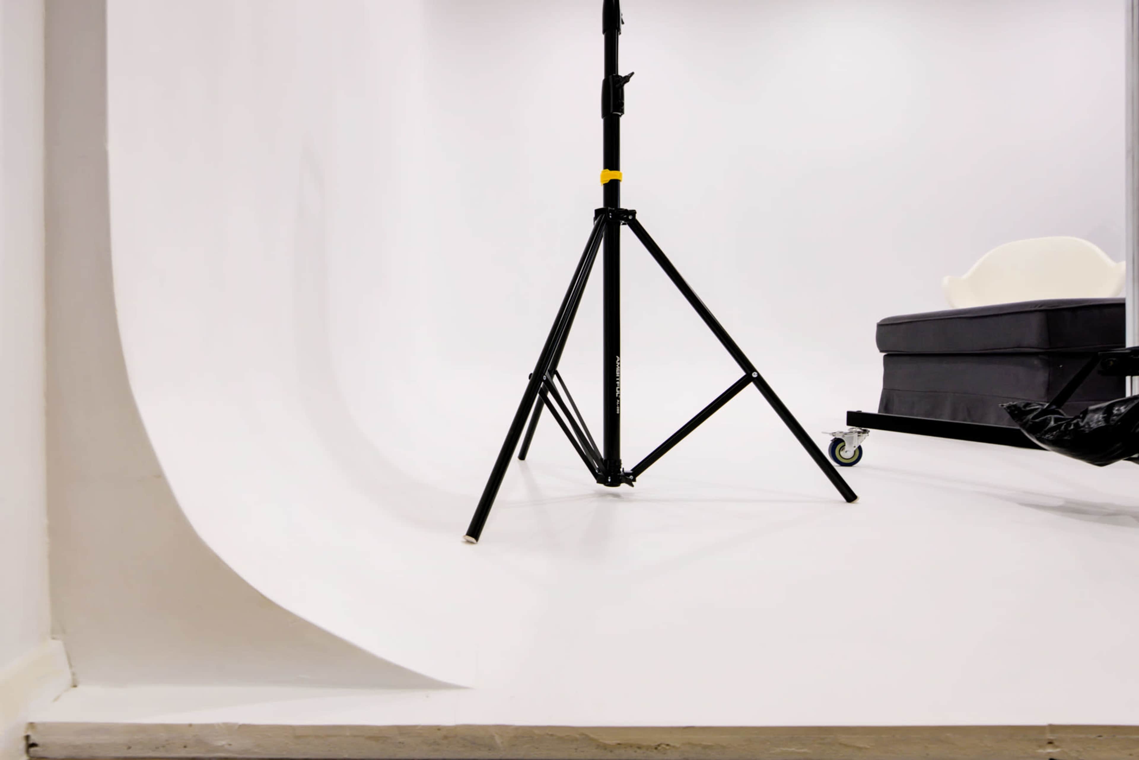 A black lighting stand supports a white backdrop in a studio setting.