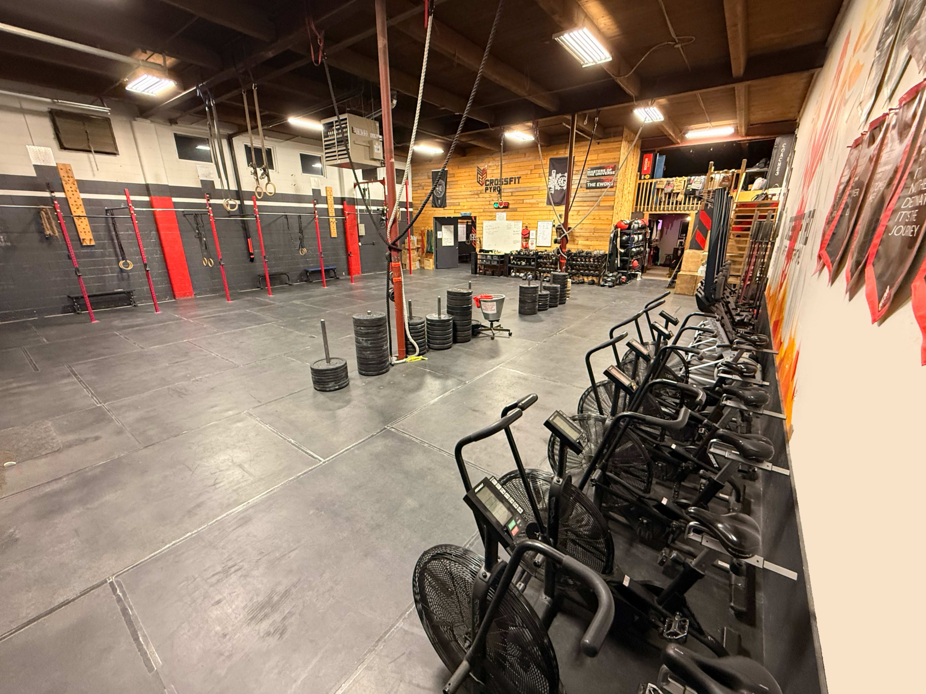 The image shows a spacious gym with exercise equipment, including air bikes lined up along one wall and various weightlifting stations in the background.