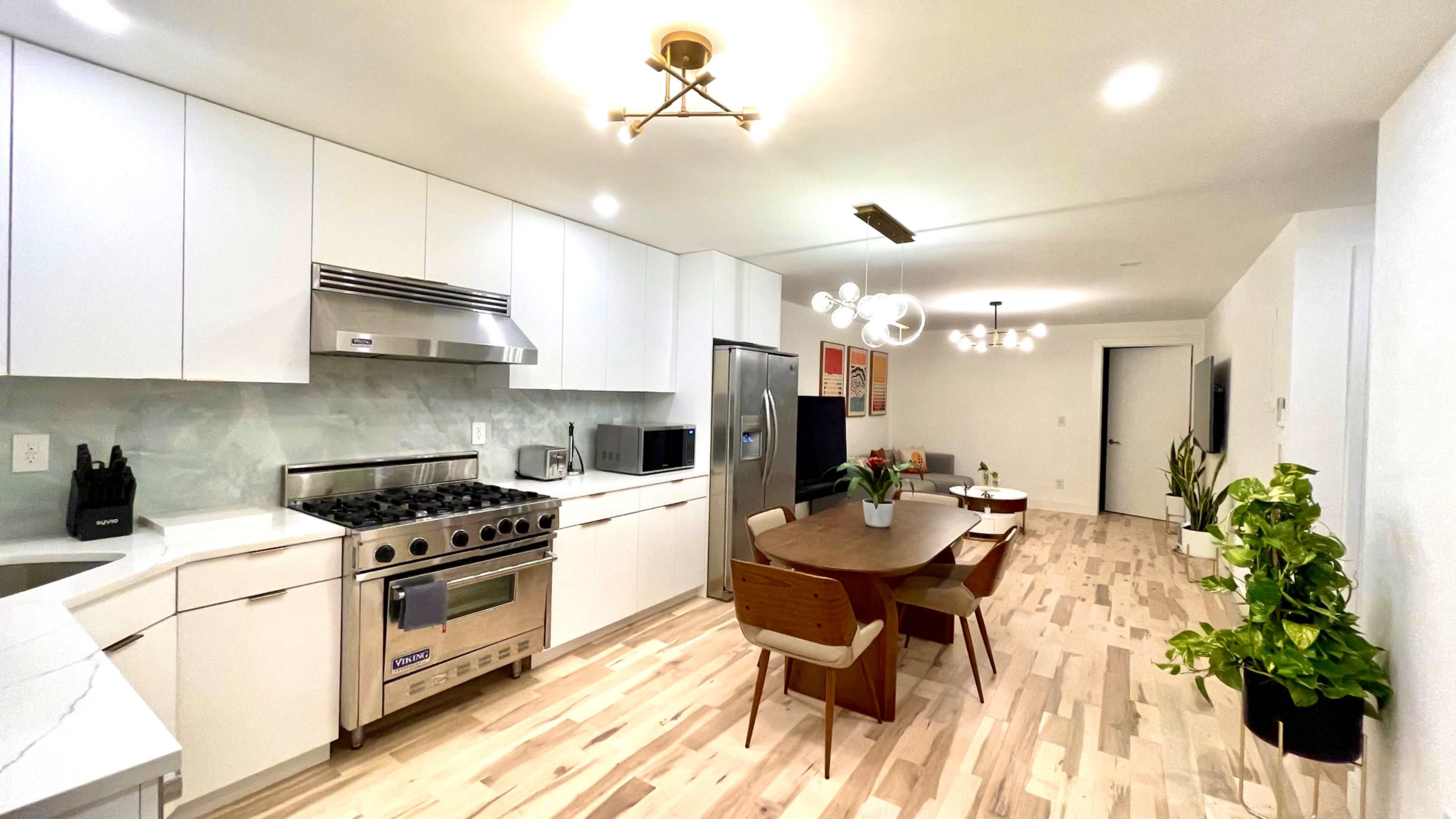 A modern kitchen features white cabinetry, stainless steel appliances, and a dining area with a round table surrounded by wooden chairs.