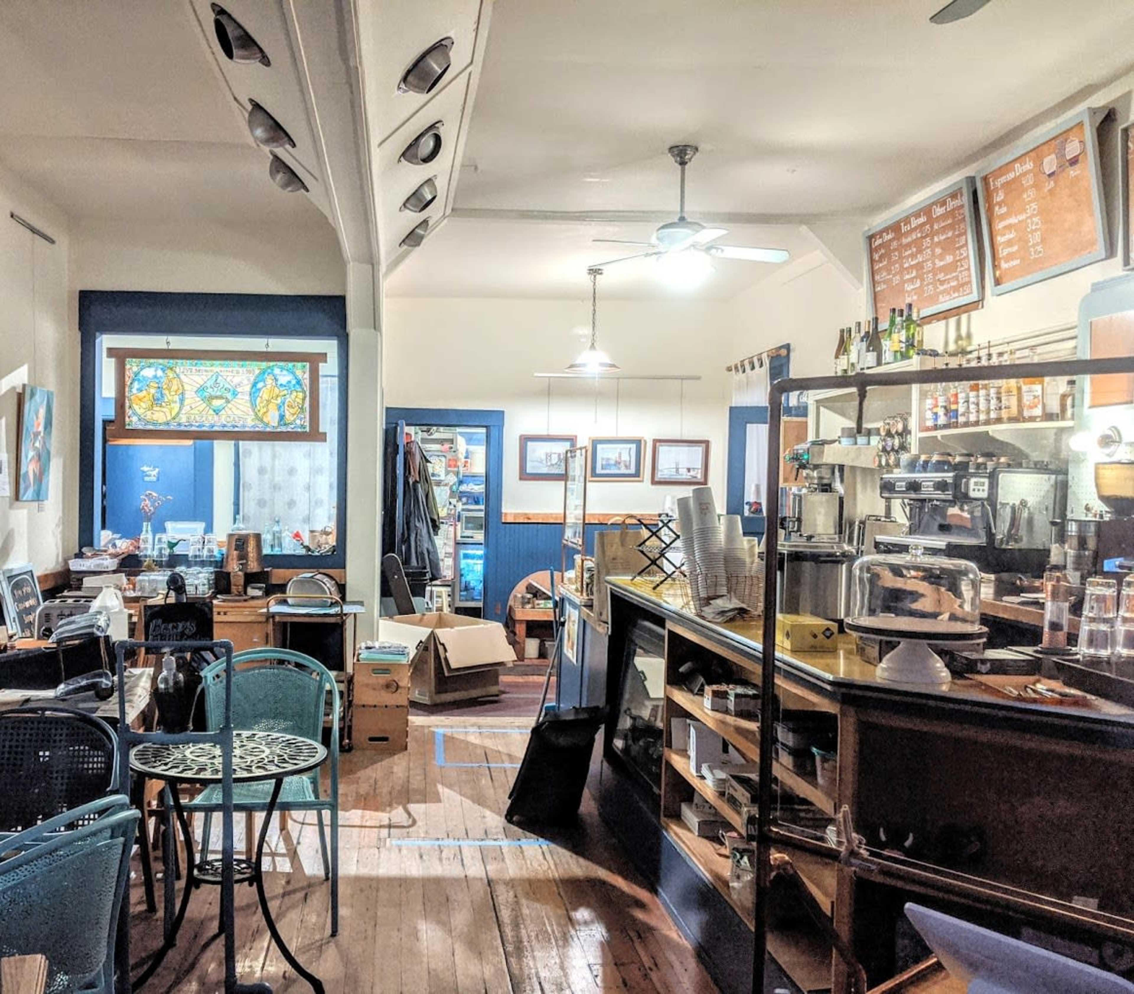 A cozy café interior with wooden floors, a counter displaying coffee equipment, and scattered tables and chairs.